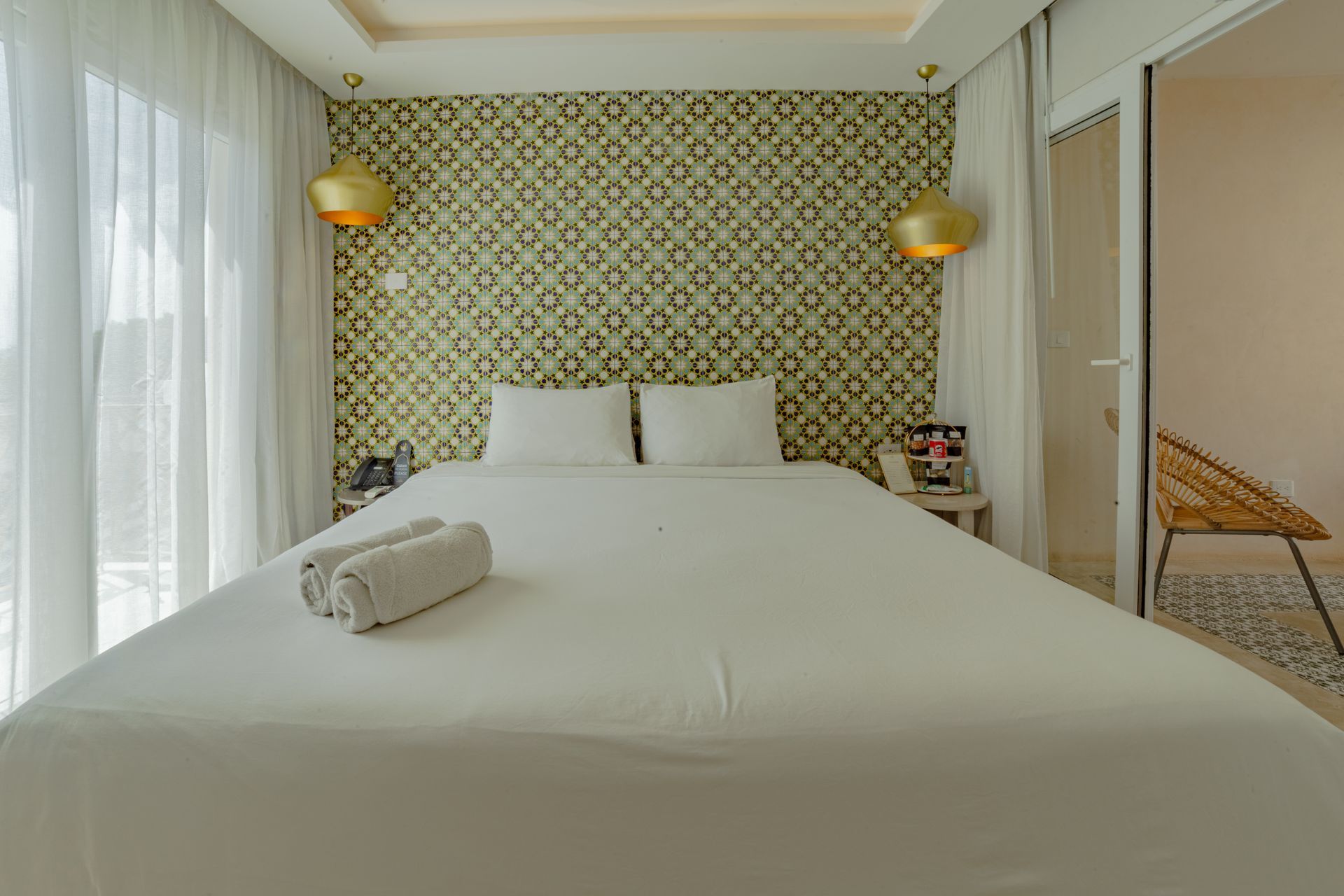 Un dormitorio con una cama blanca, papel tapiz verde estampado y lámparas doradas.