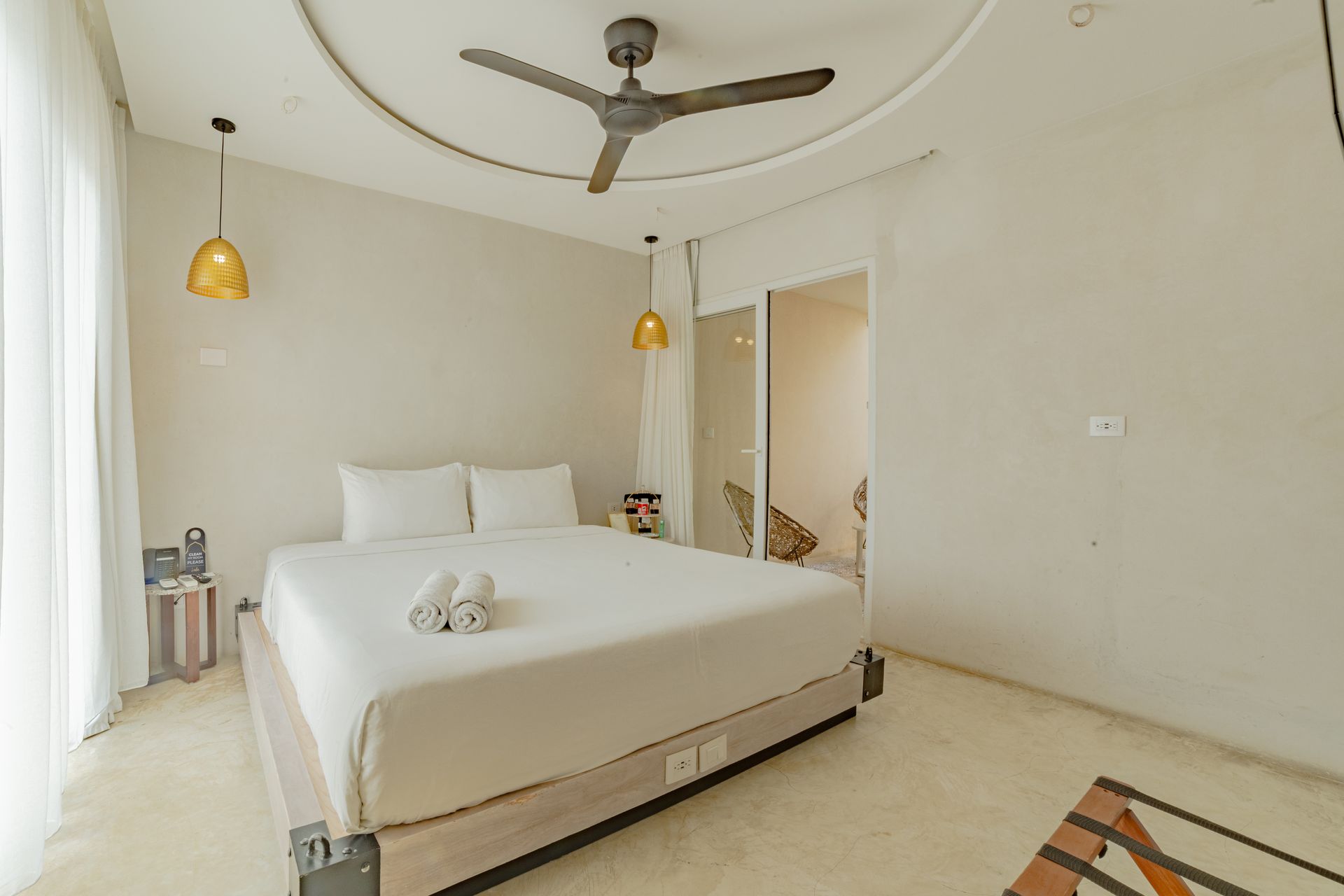 Dormitorio con cama, ventilador de techo y lámparas colgantes; tonos neutros.