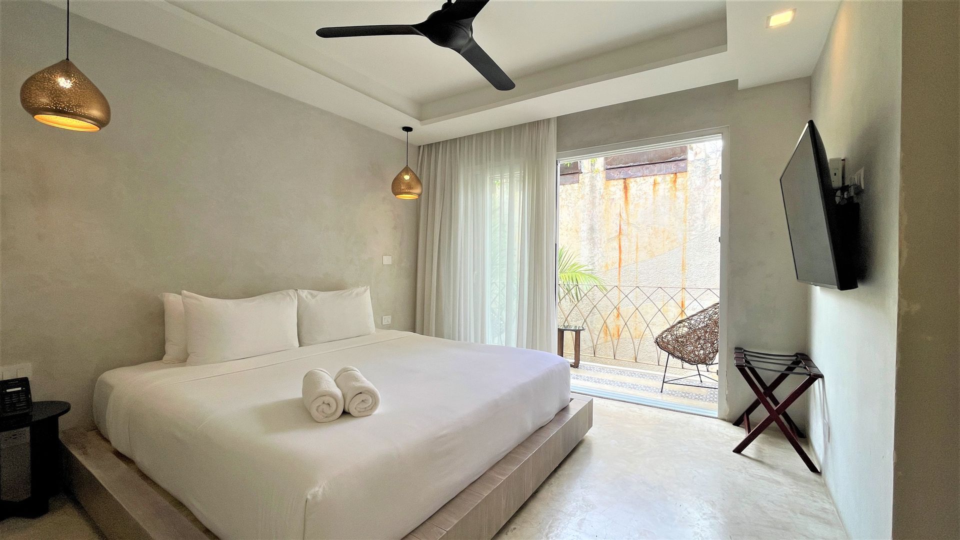 Una habitación de hotel con una cama grande, ventilador de techo, televisión y balcón.