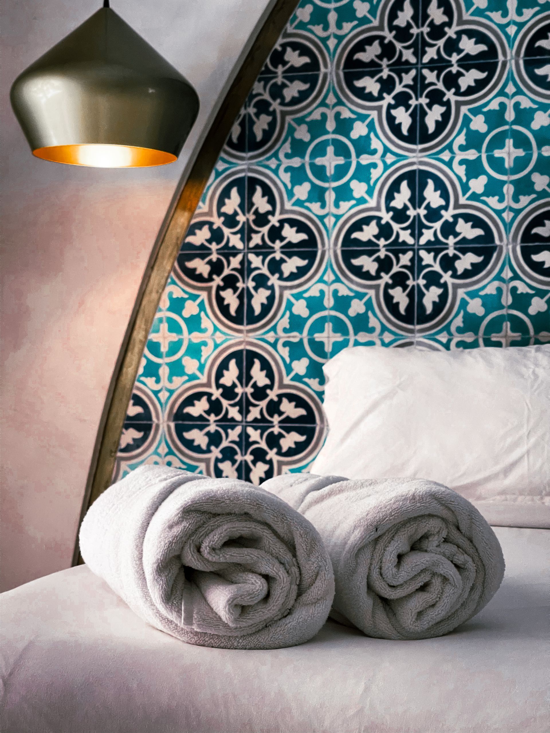 Dos toallas están enrolladas sobre una cama frente a una pared de azulejos.