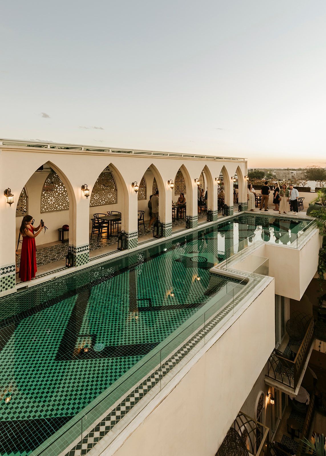 Una mujer con un vestido rojo está parada junto a una gran piscina.