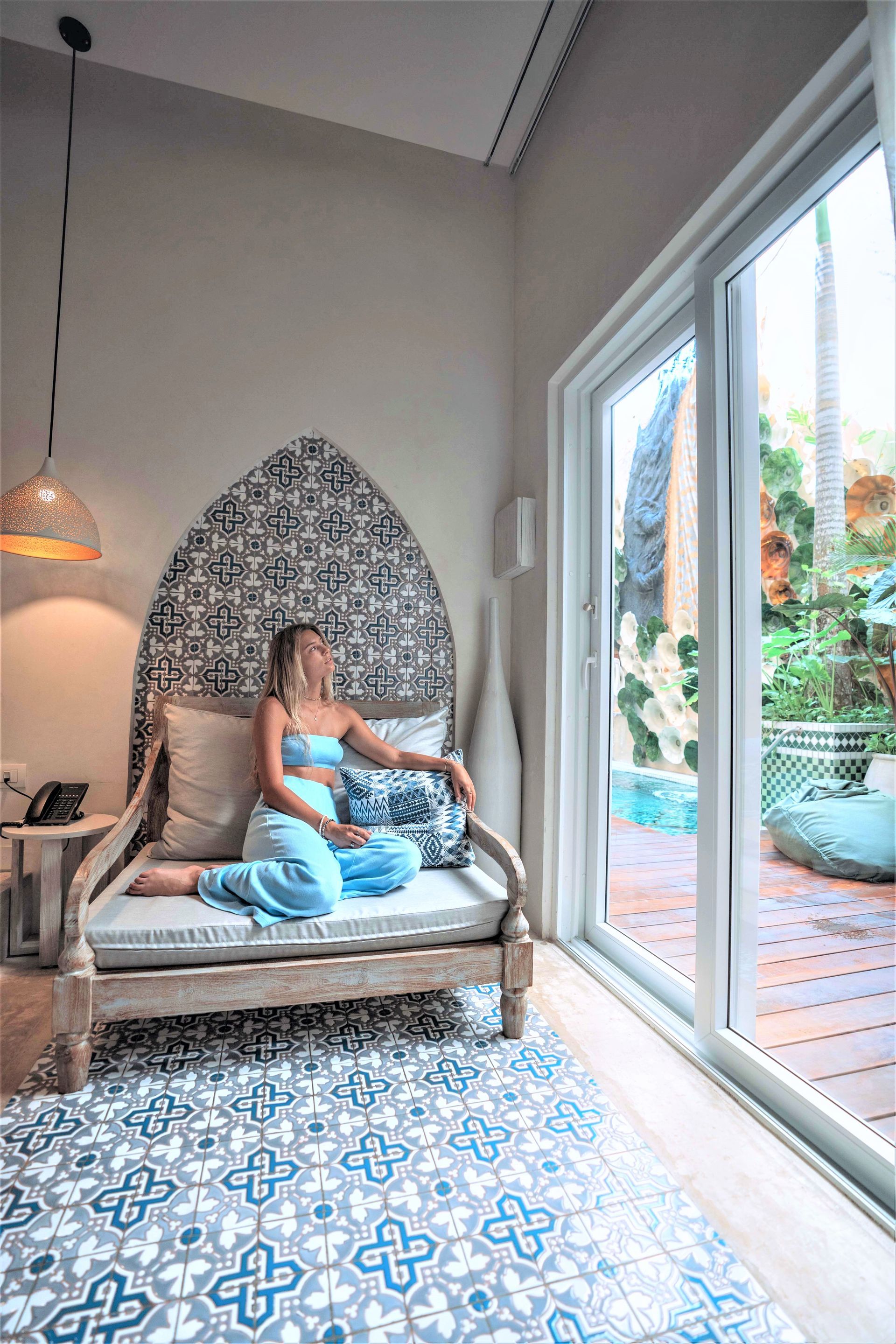 Una mujer está sentada en un sofá en una habitación al lado de una ventana.