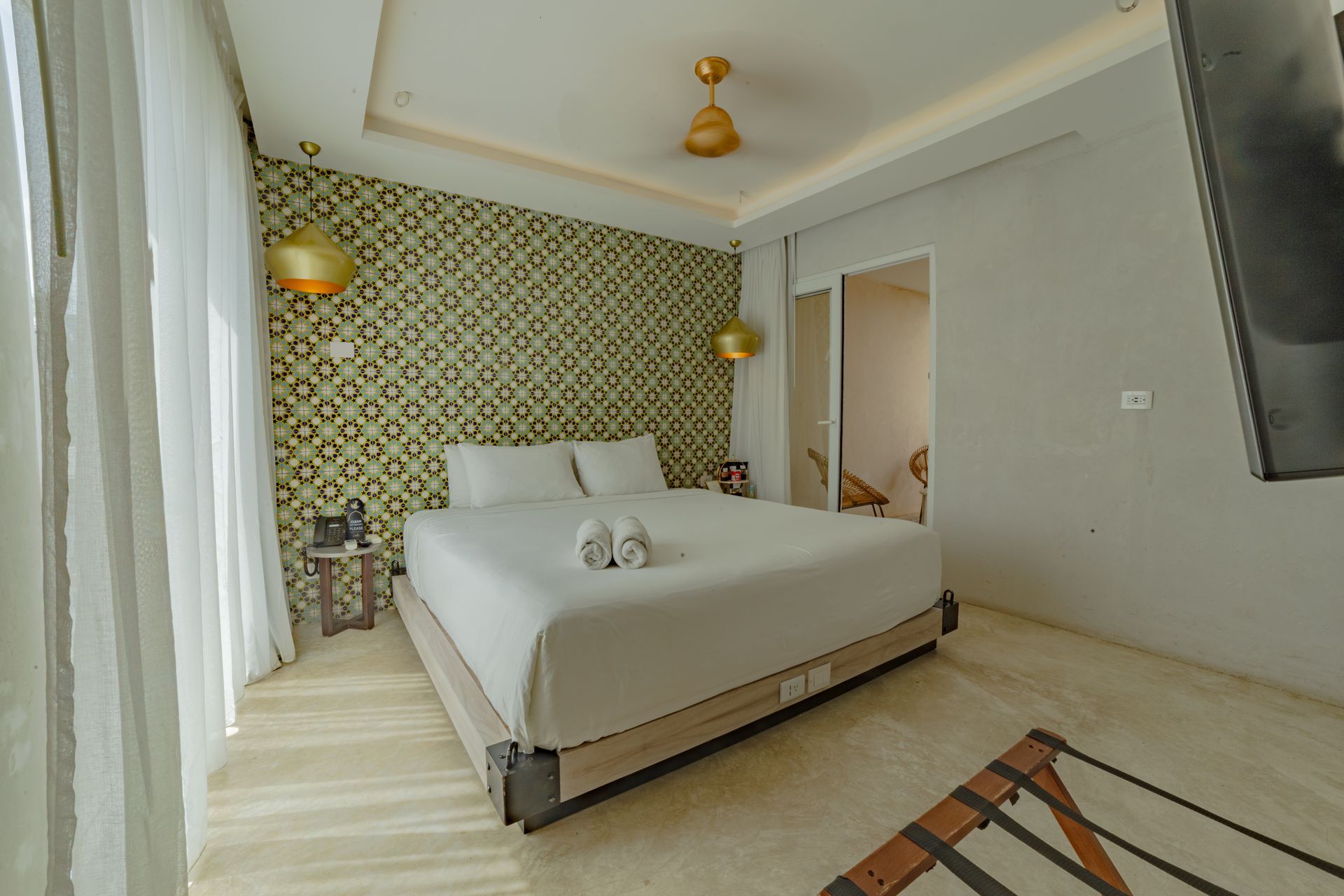 Dormitorio con cama tamaño king, pared estampada, dos apliques dorados y una puerta que conduce a un baño.