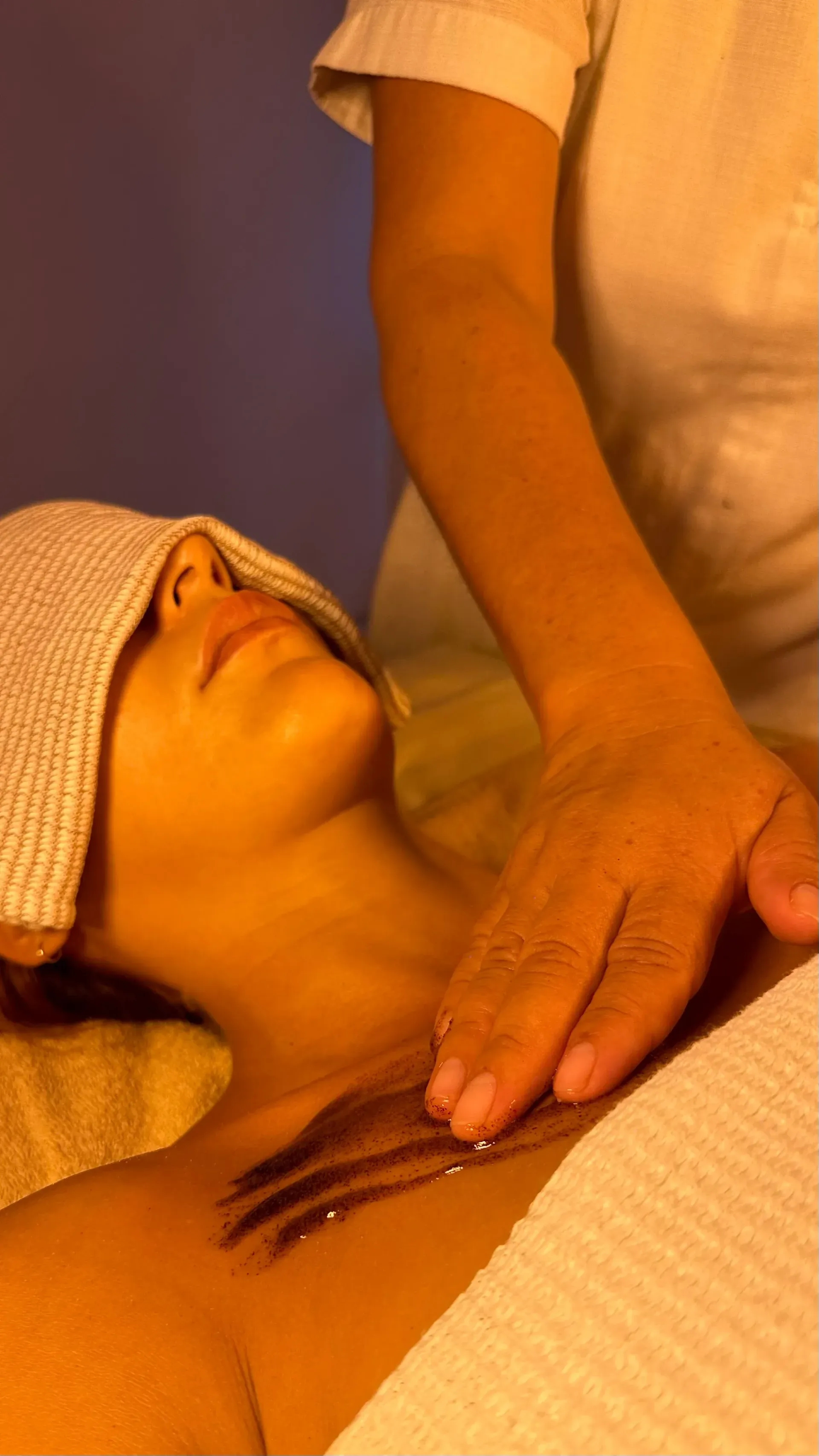 Mujer recibiendo un masaje de pecho, tratamiento de spa. Aplica exfoliante en las manos y cubre los ojos con una toalla.