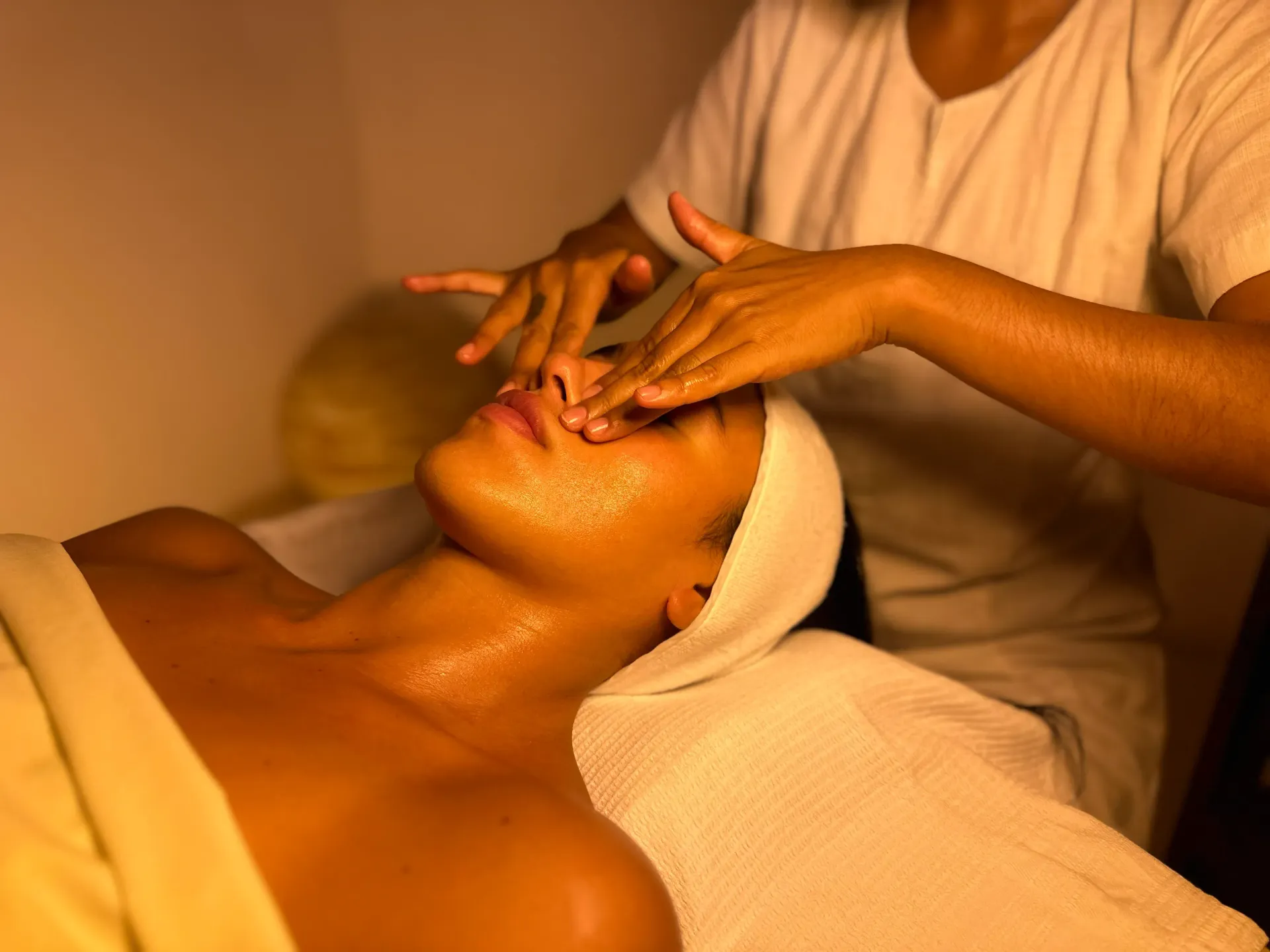 Persona recibiendo un masaje facial en un spa; la masajista aplica presión en la cara y la frente.