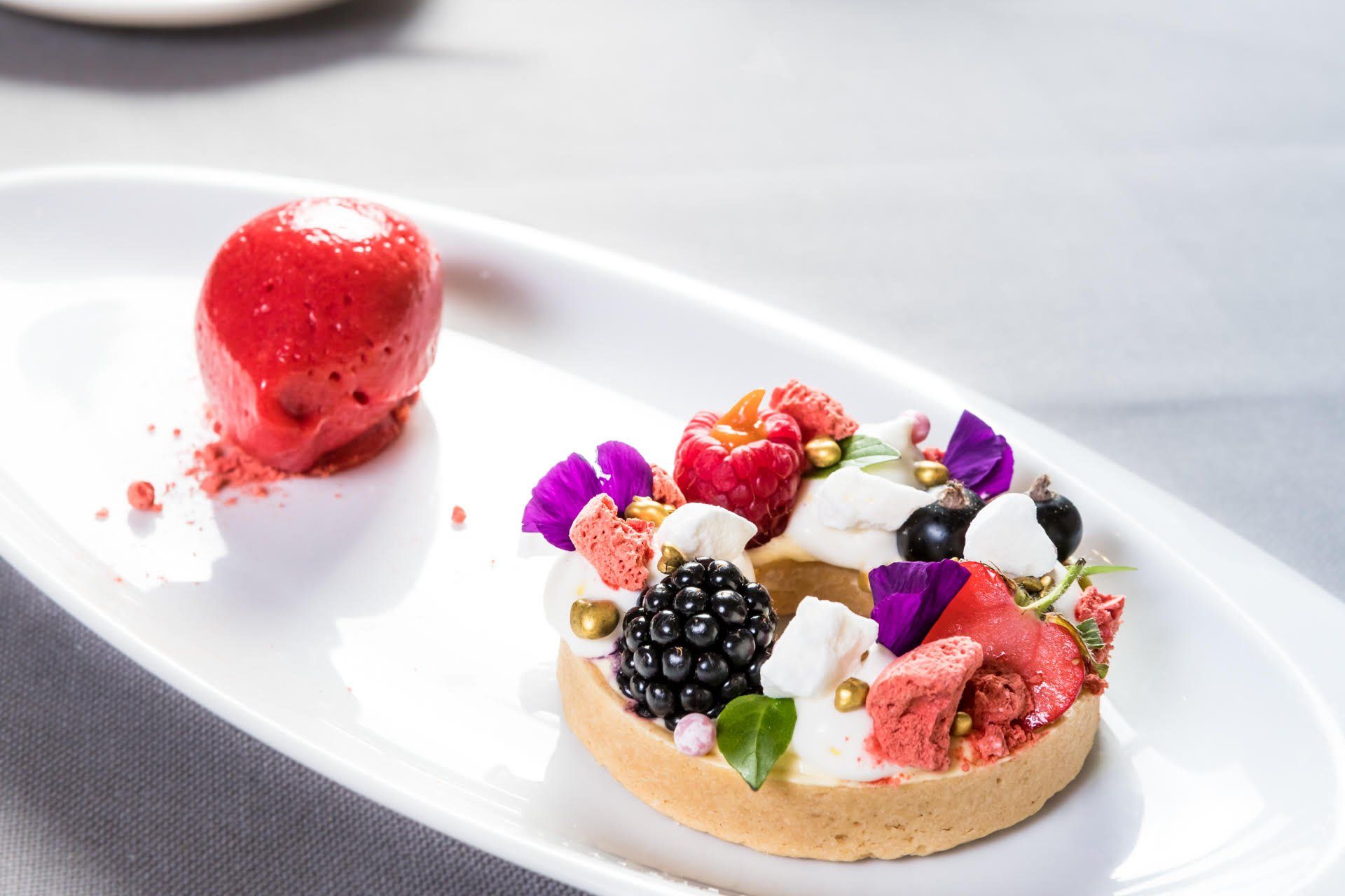 Auf einem Tisch steht ein weißer Teller mit einem Dessert und einer Erdbeere.