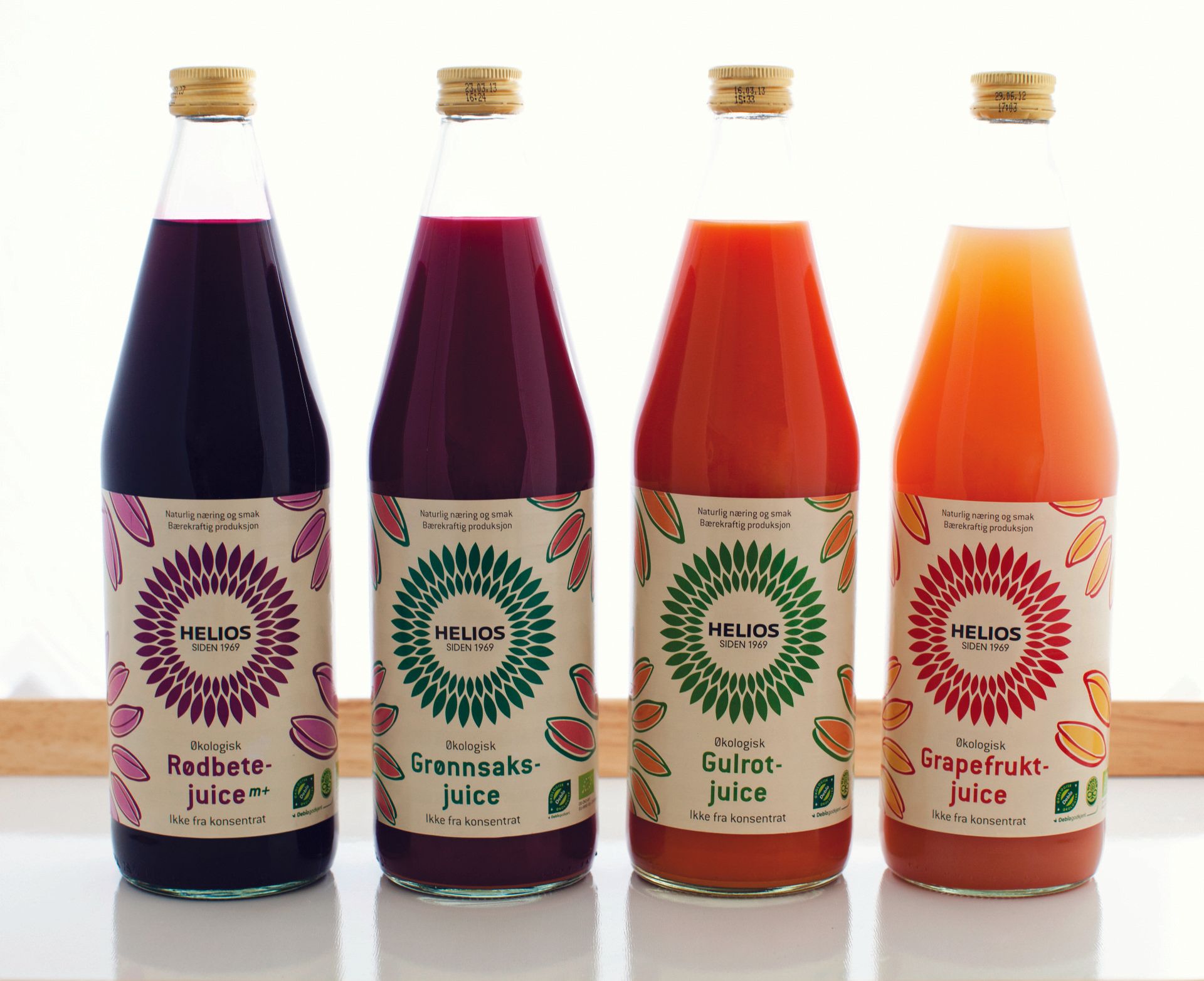 Fire flasker med forskjellige juicer står på rekke og rad på et bord