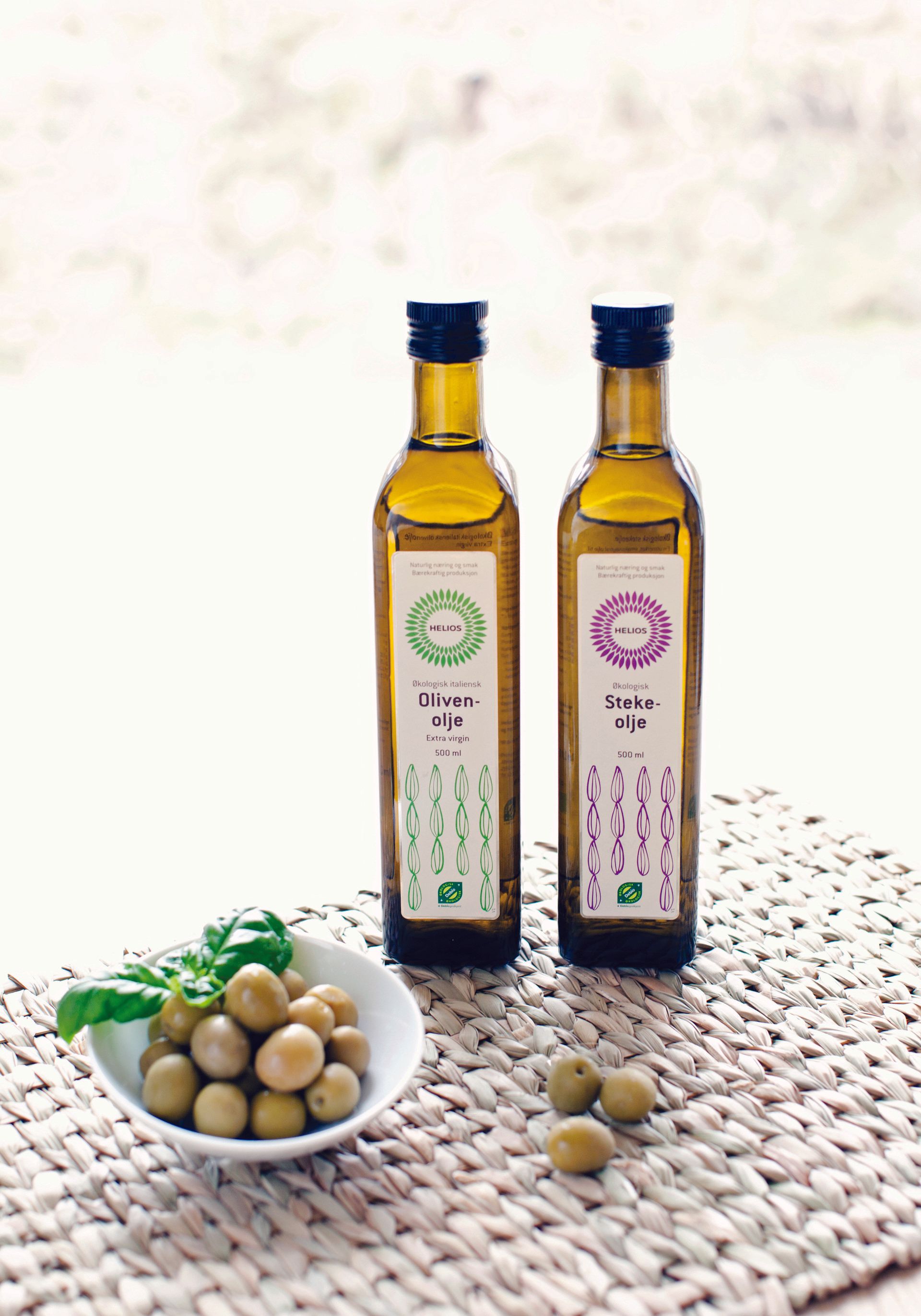 To flasker olivenolje står på et bord ved siden av en skål med oliven.
