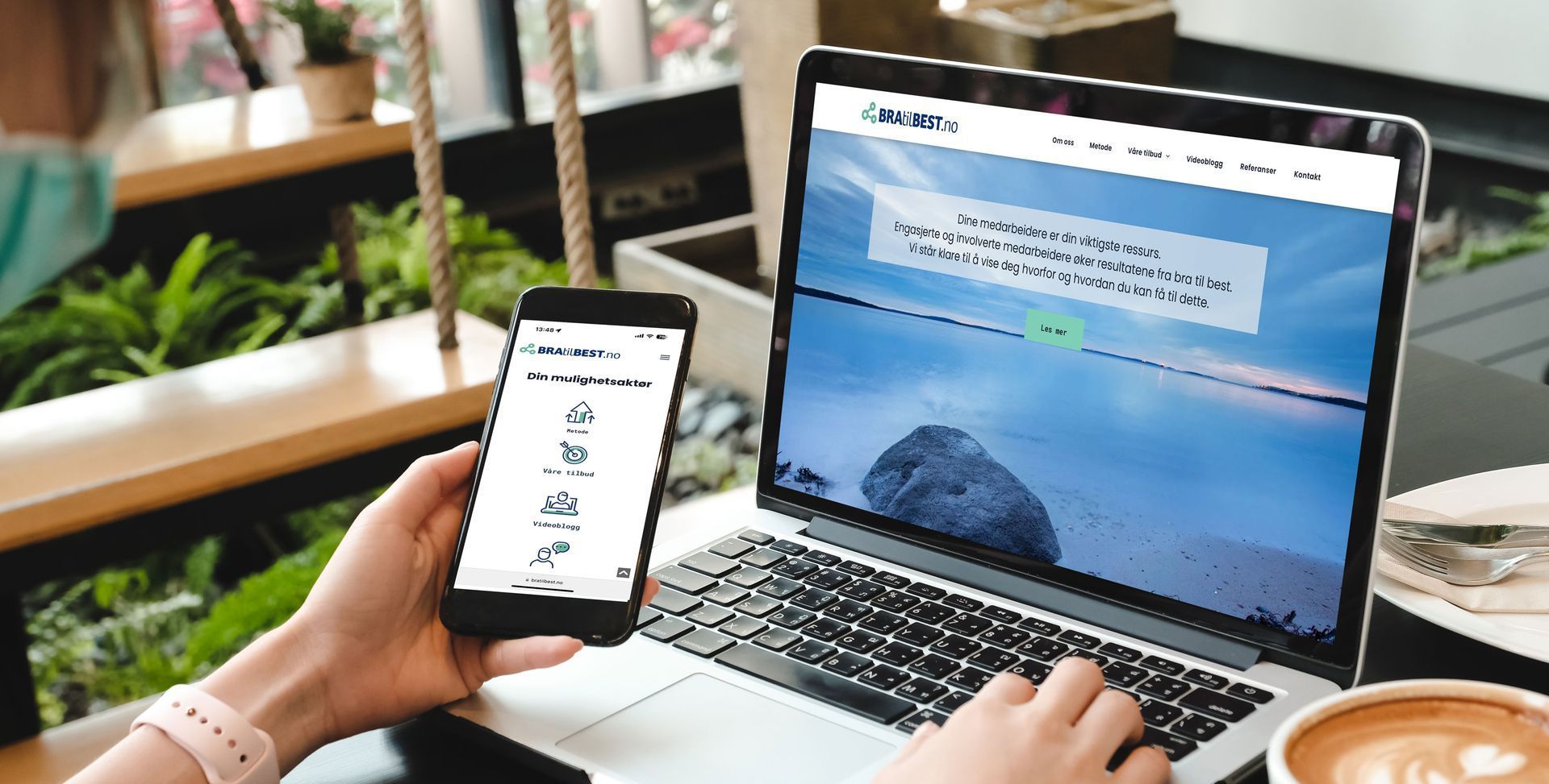 En person holder en mobiltelefon foran en bærbar datamaskin.