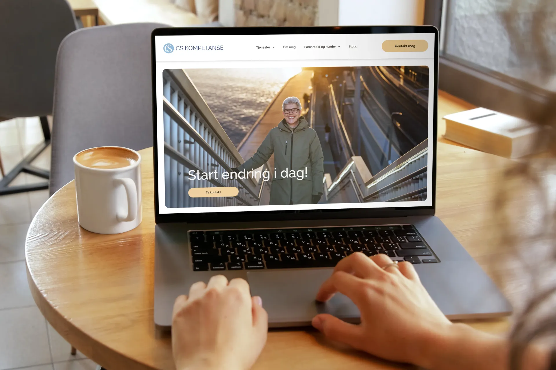 Person som bruker en bærbar PC og viser en nettside med en mann i en grønn jakke. En kopp kaffe på et bord.