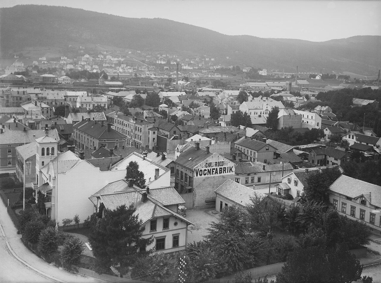 Bylandskap med bygninger og fjell i bakgrunnen. Svart og hvitt.