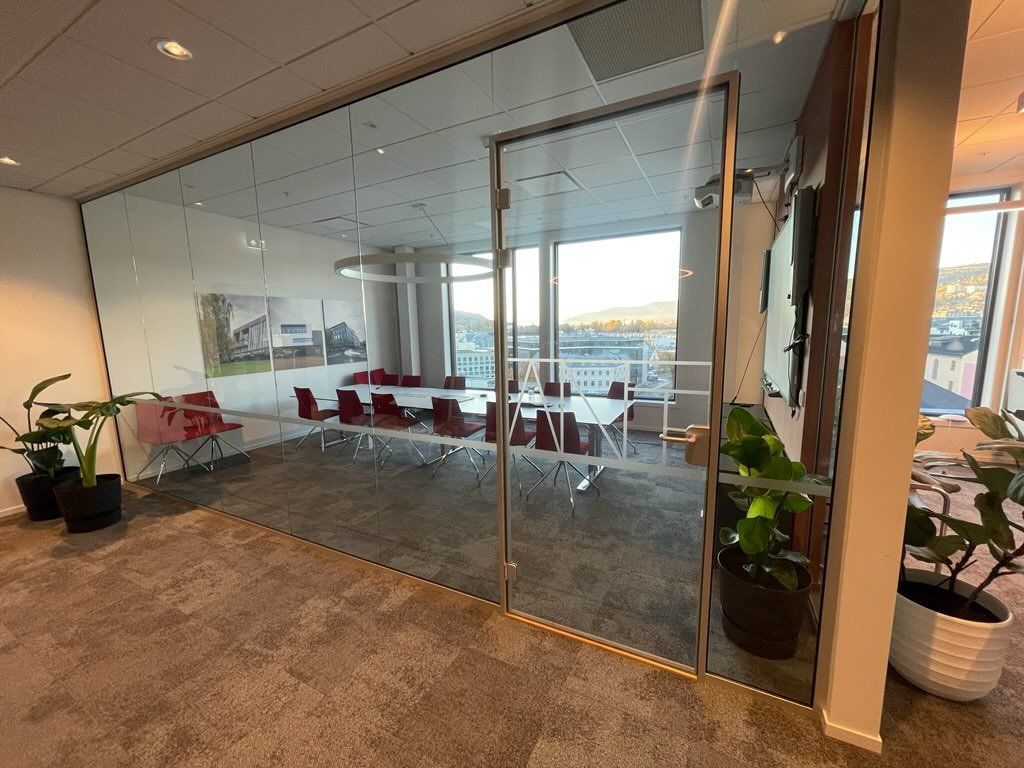 Et konferanserom med glassvegg og bord og stoler.