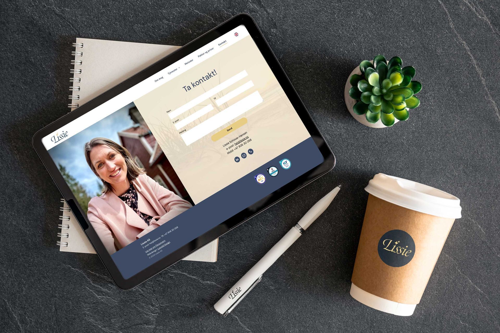 Et nettbrett ligger på et bord ved siden av en kopp kaffe og en penn.