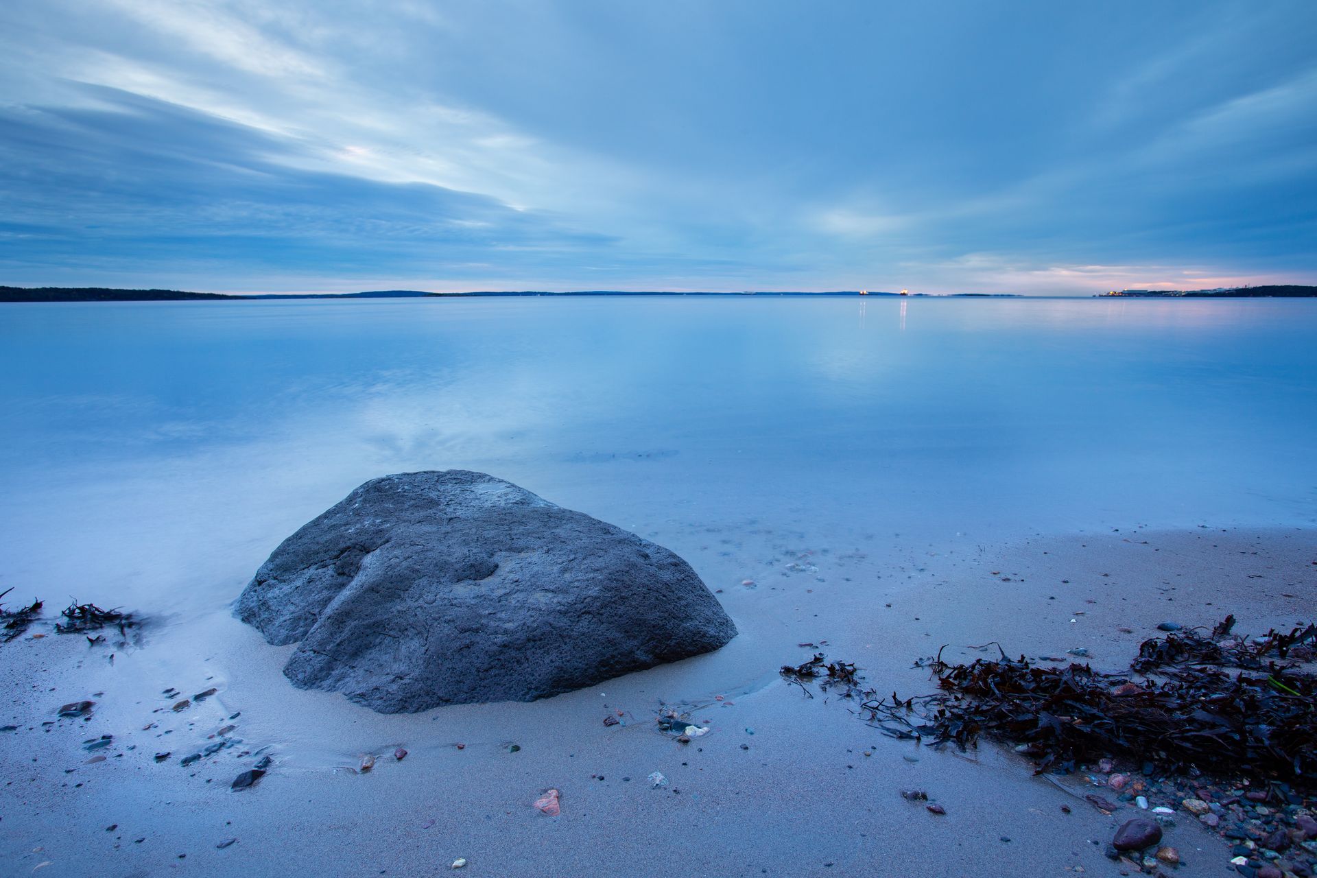 En stor stein ligger på en sandstrand nær havet.