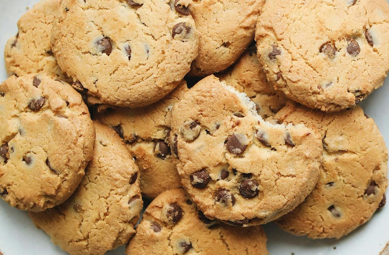 Pile of golden-brown chocolate chip cookies, some with visible chips, one partially eaten.