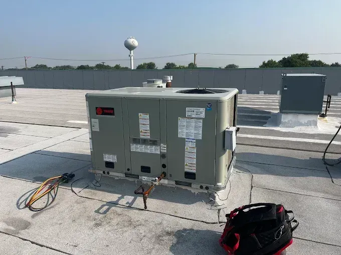 Commercial rooftop HVAC unit with cables and tool bag on a flat roof under a clear sky