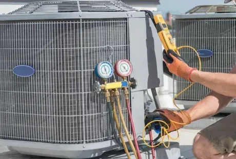 Technician using gauges and hoses to service a rooftop HVAC unit