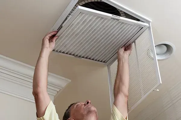 Person changing a ceiling vent filter overhead in a home interior