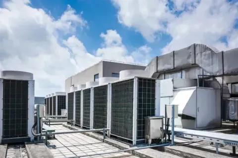 Rooftop HVAC units and ductwork against a partly cloudy blue sky.
