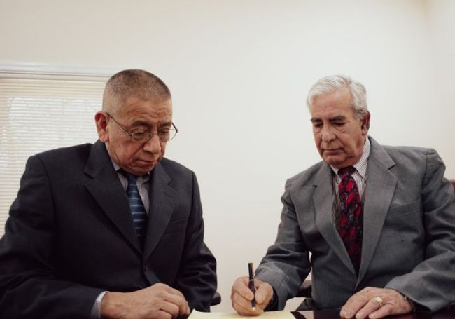 Two men in suits and ties are sitting at a table signing a document.