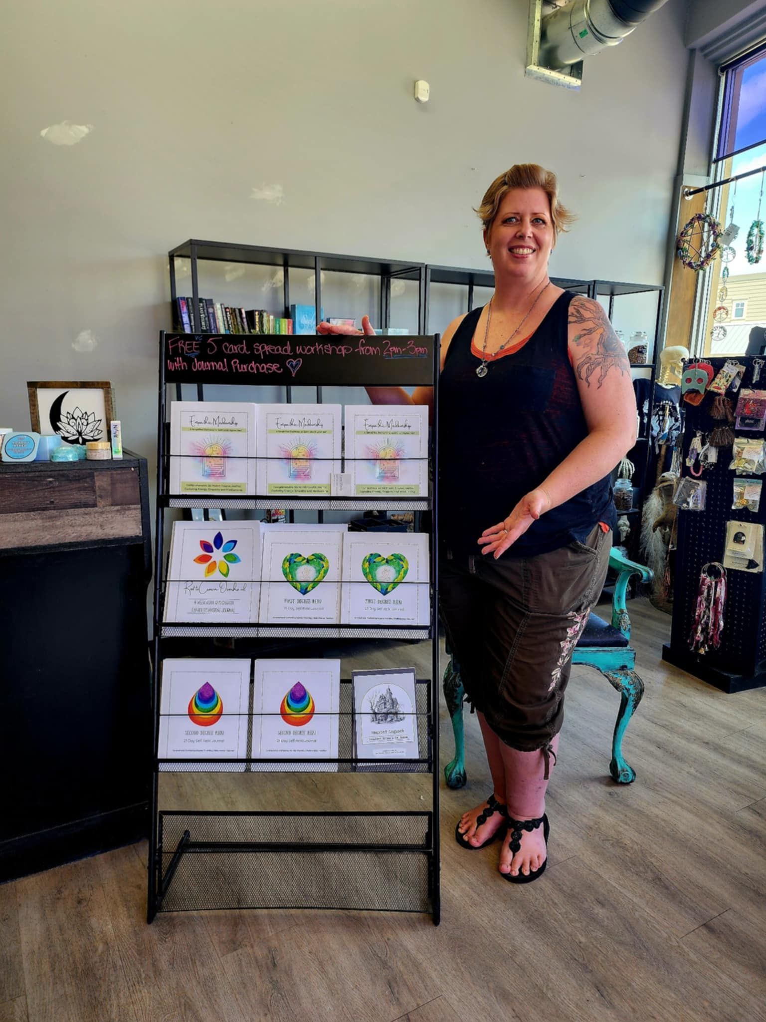 Woman in a shop stands next to a display of greeting cards; shop has blue and gray accents, a teal chair.