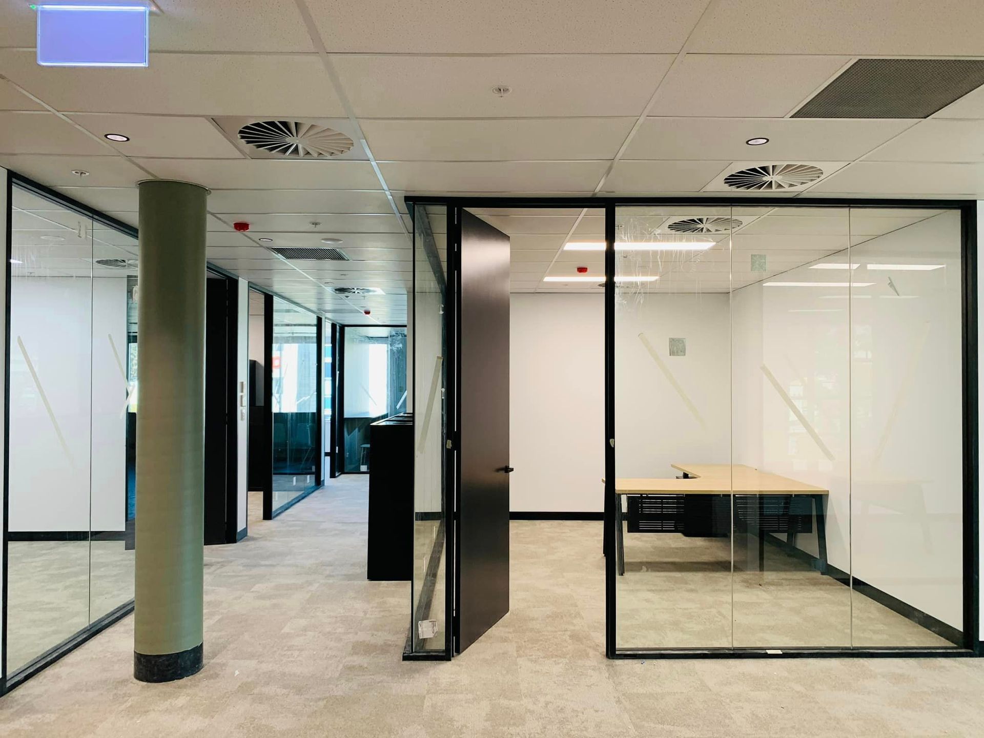 An empty office with a glass wall and a desk.
