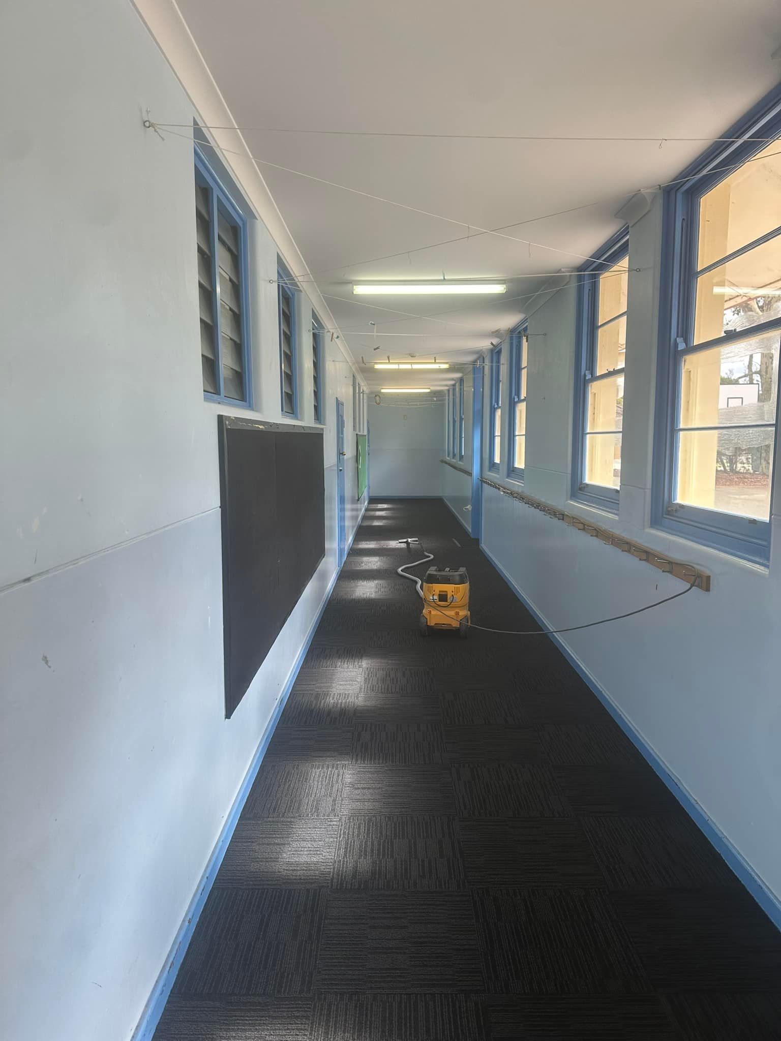 A long hallway with a lot of windows and a yellow bucket on the floor.