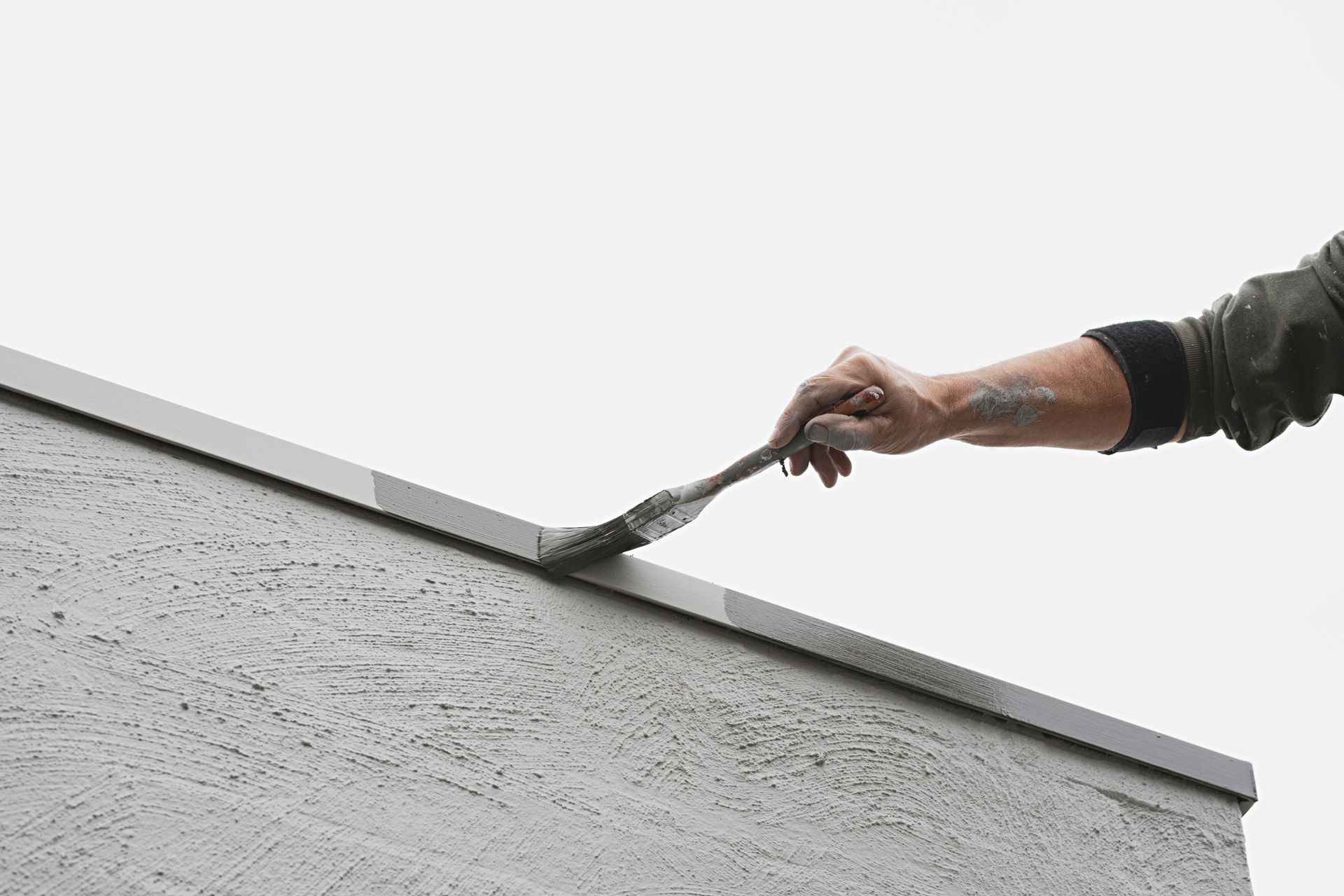 View of the hand of a painter painting the outdoor rim of a house with a brush.