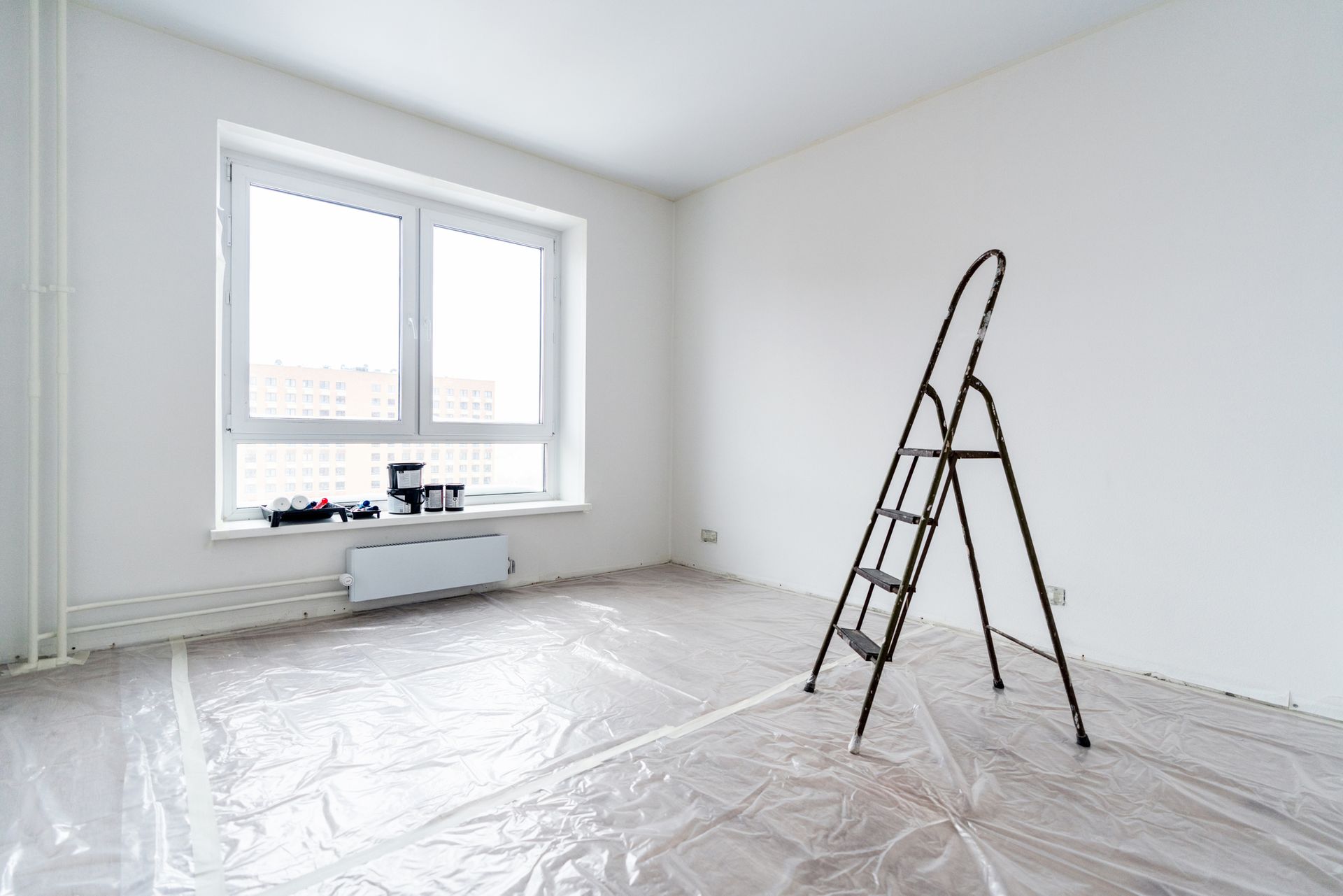 An empty room prepared for commercial painting services, with the floor covered in polythene. An empty room prepared for commercial painting services, with the floor covered in polythene.