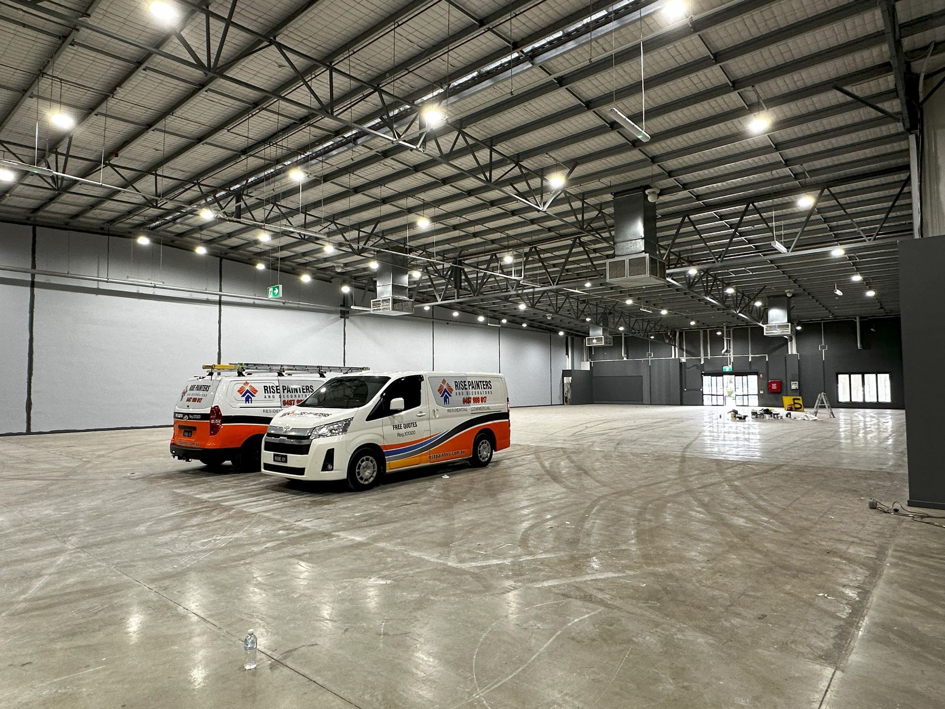 Two service vans parked inside a large, empty warehouse with bright overhead lights.