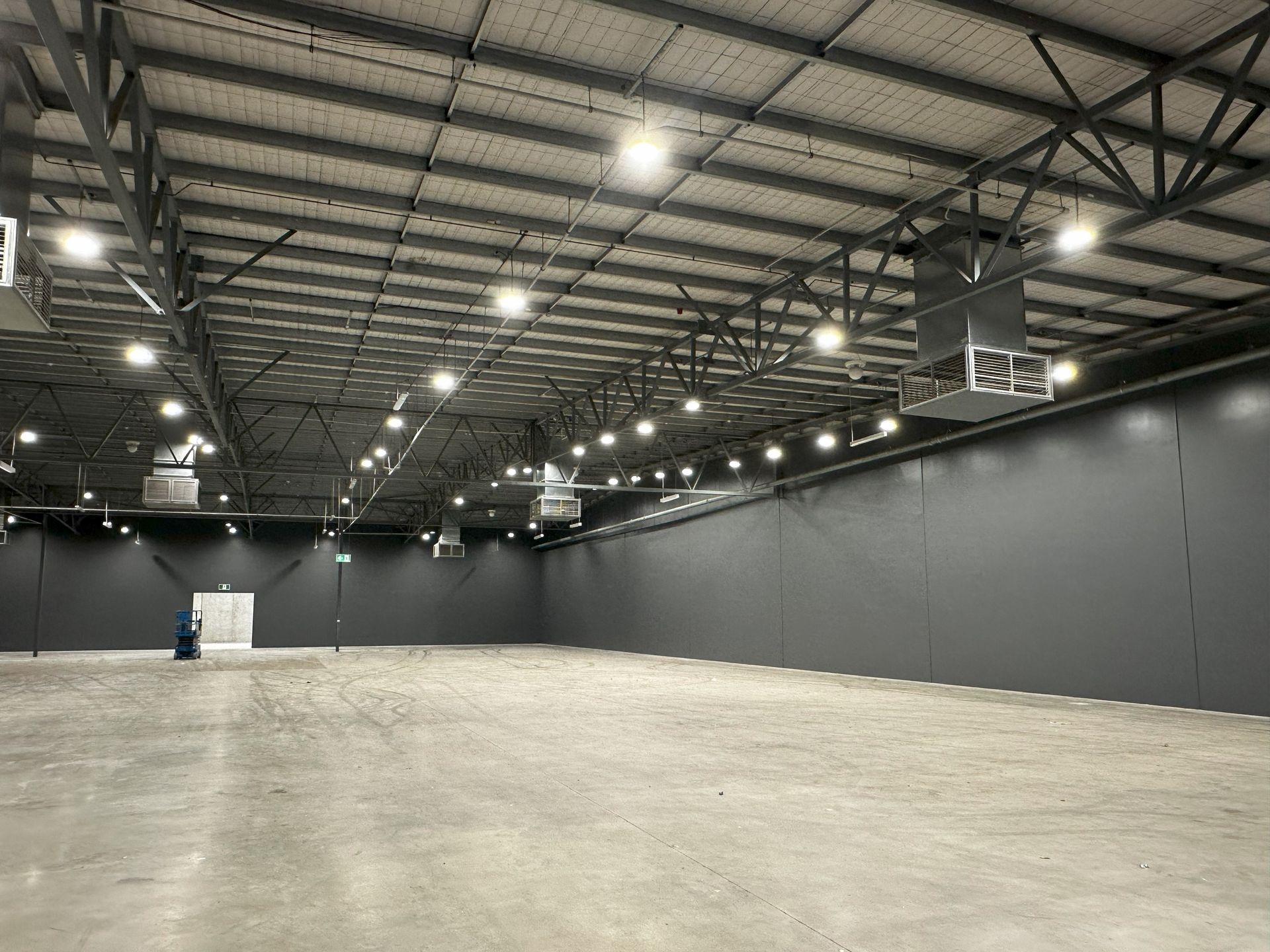 Large, empty warehouse with gray walls and ceiling, and overhead lighting.