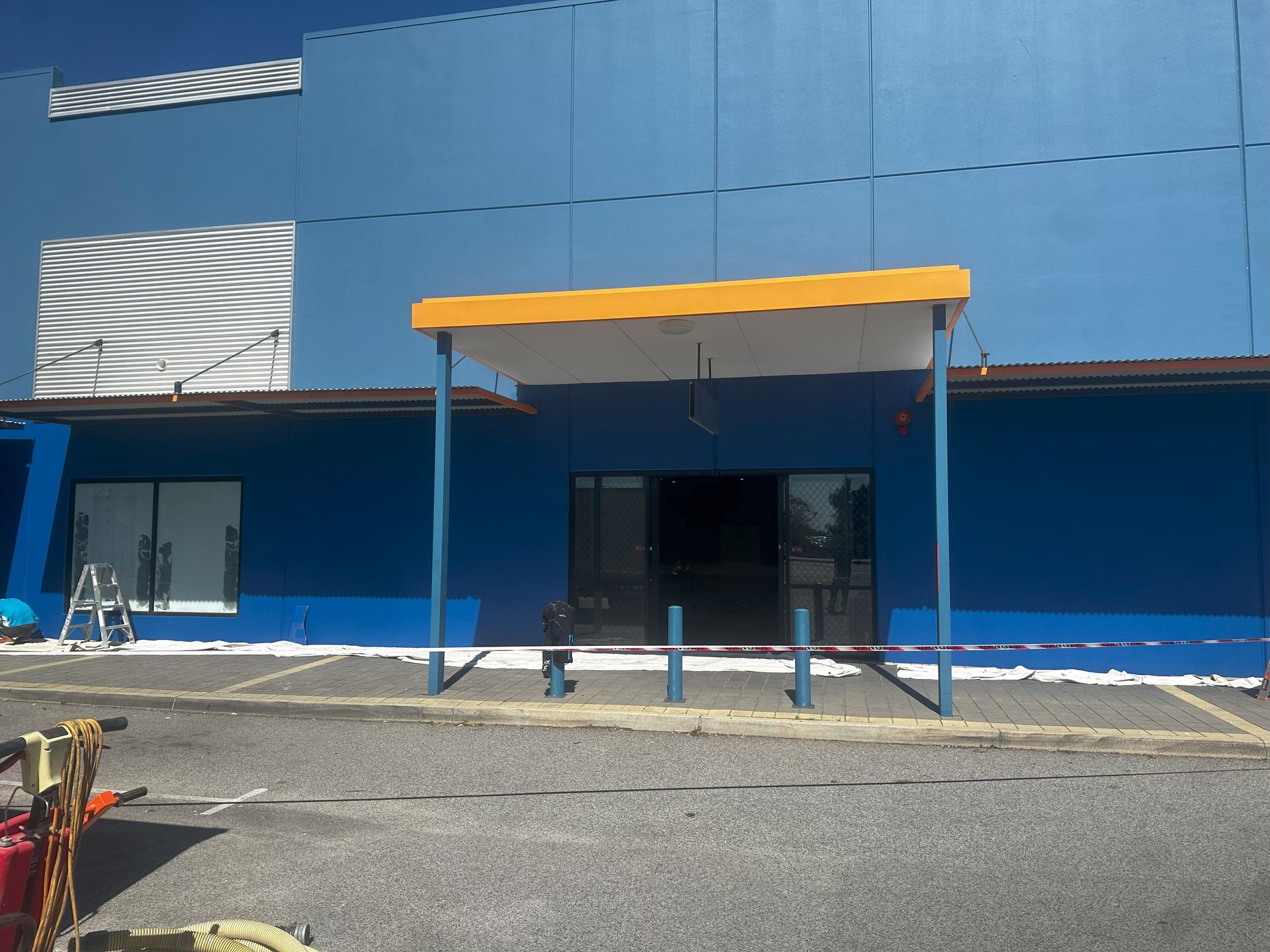 Blue building with yellow awning over entrance; blue poles and white trim.