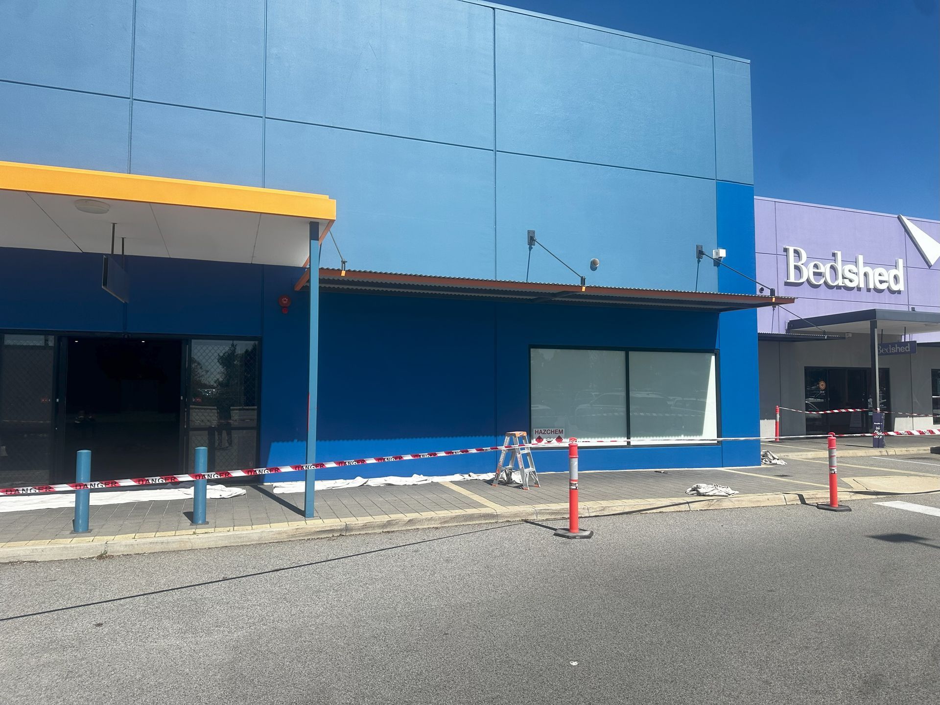 Exterior of blue building with broken awning, construction tape; Bed Shed sign in background.