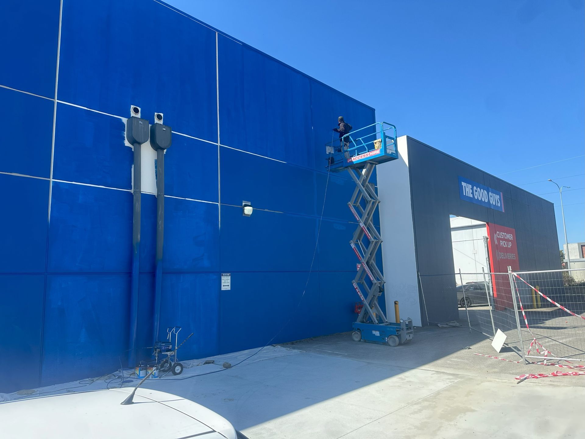 A worker on a blue lift works on the blue exterior of a building. Bright blue sky.