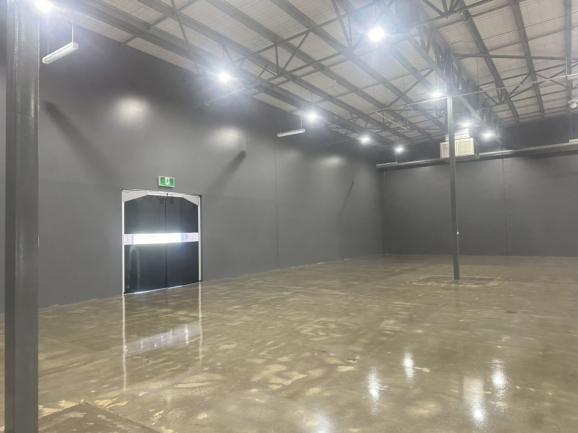 Empty industrial space with dark gray walls, concrete floor, and bright overhead lights.