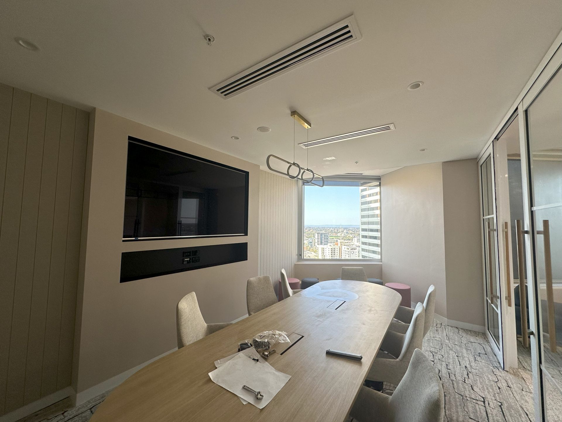 Conference room with long table, chairs, large TV, and city view through the window.