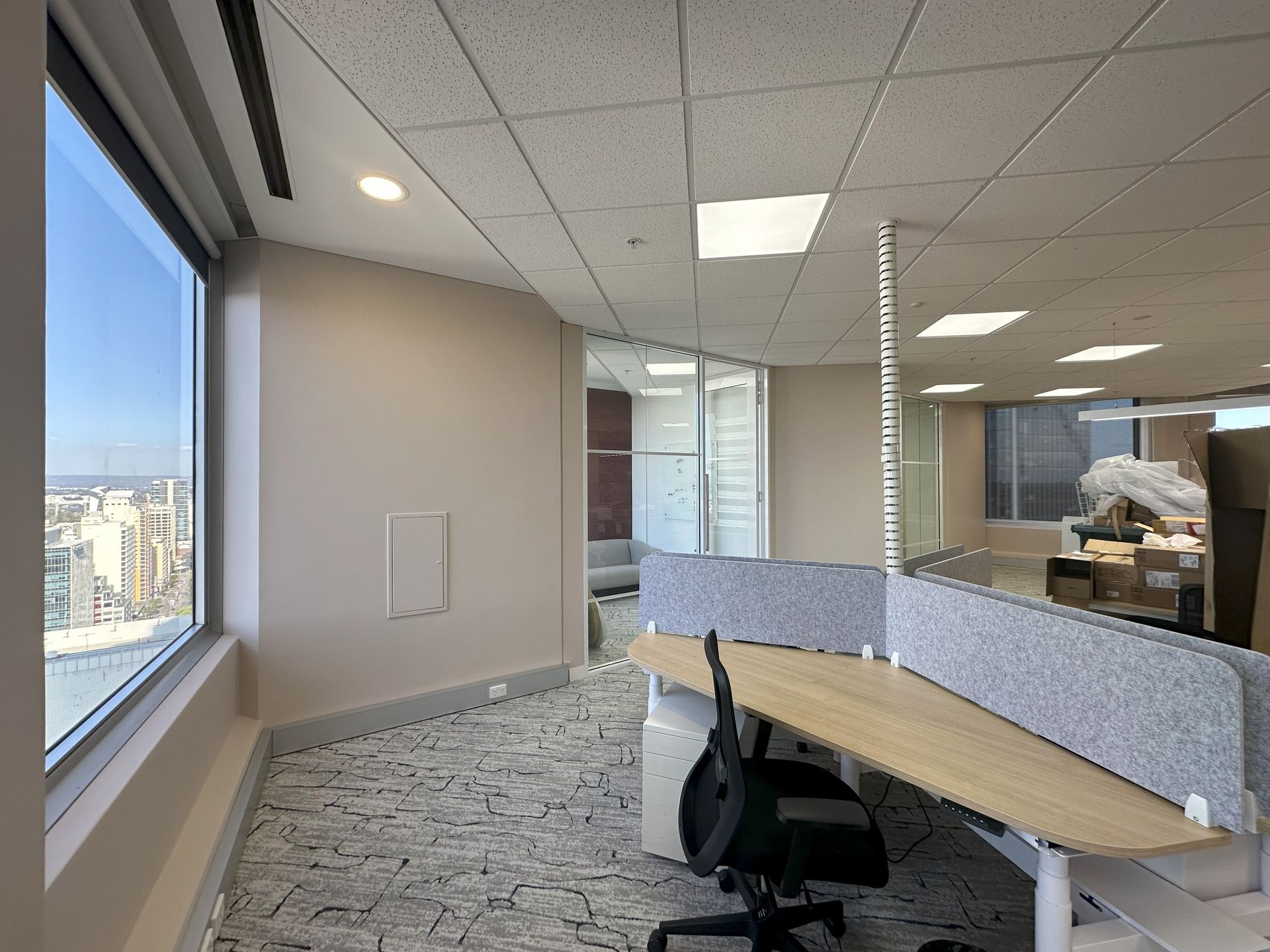 Office space with desk, window, and city view. Beige walls, patterned carpet, and gray dividers.