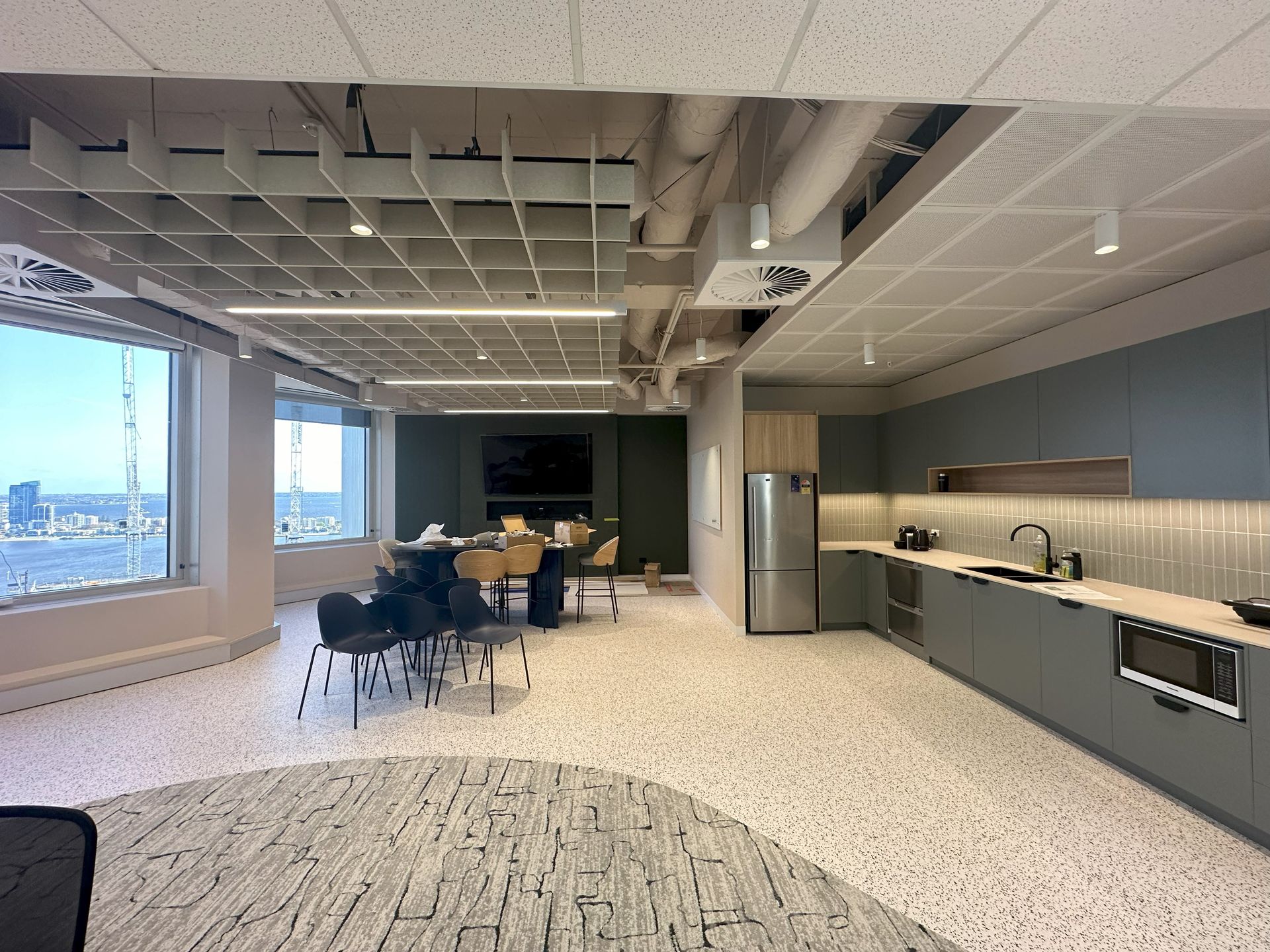 Modern office kitchen and meeting area with a view, featuring a kitchenette and meeting table.