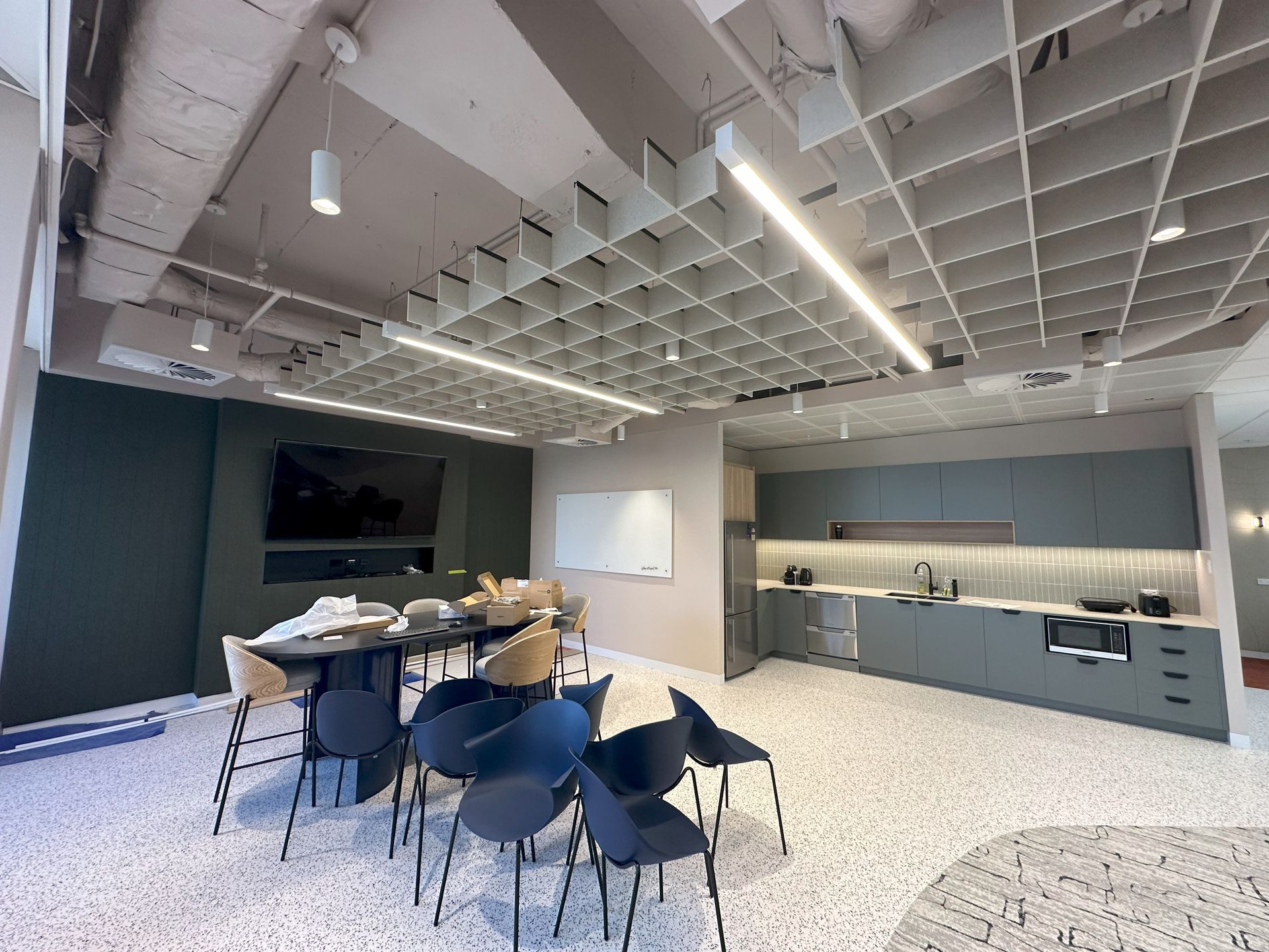 Modern office kitchen and meeting area with a gray and white color scheme. Includes a kitchen, tables, and chairs.
