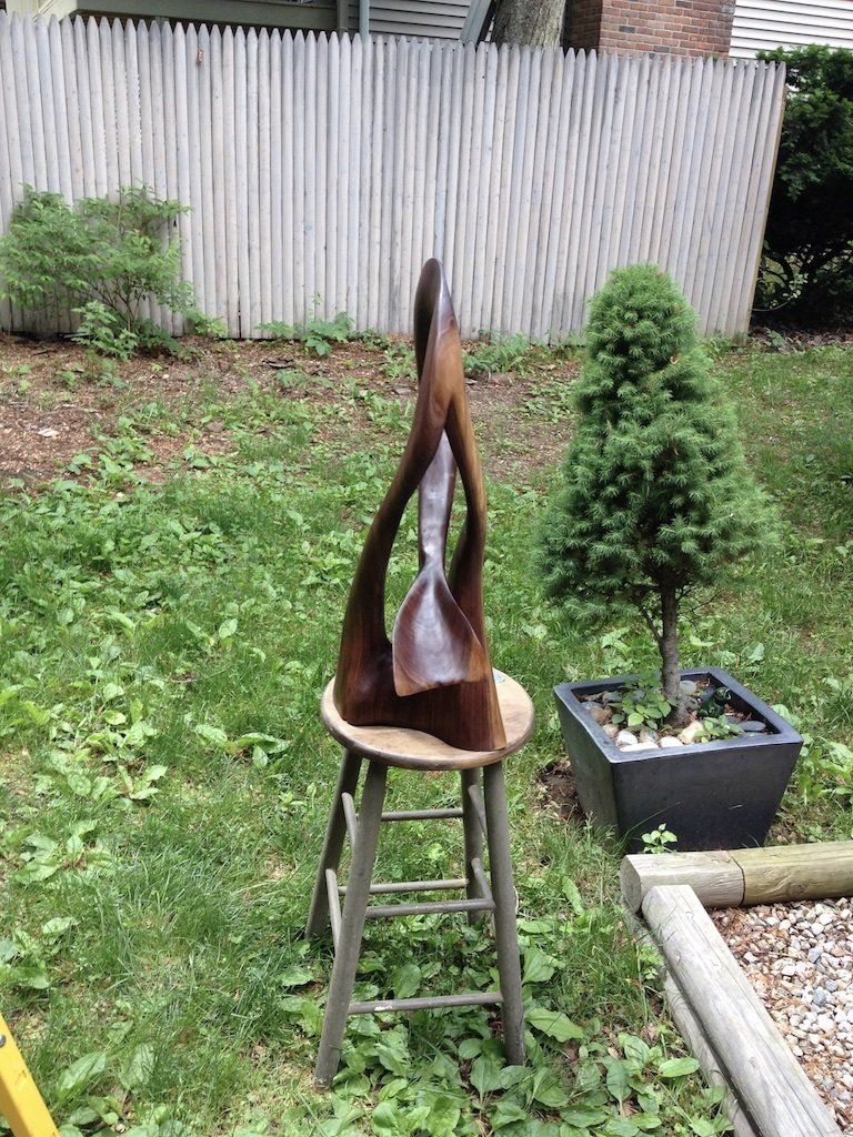 A wooden sculpture is sitting on top of a wooden stool in a yard.
