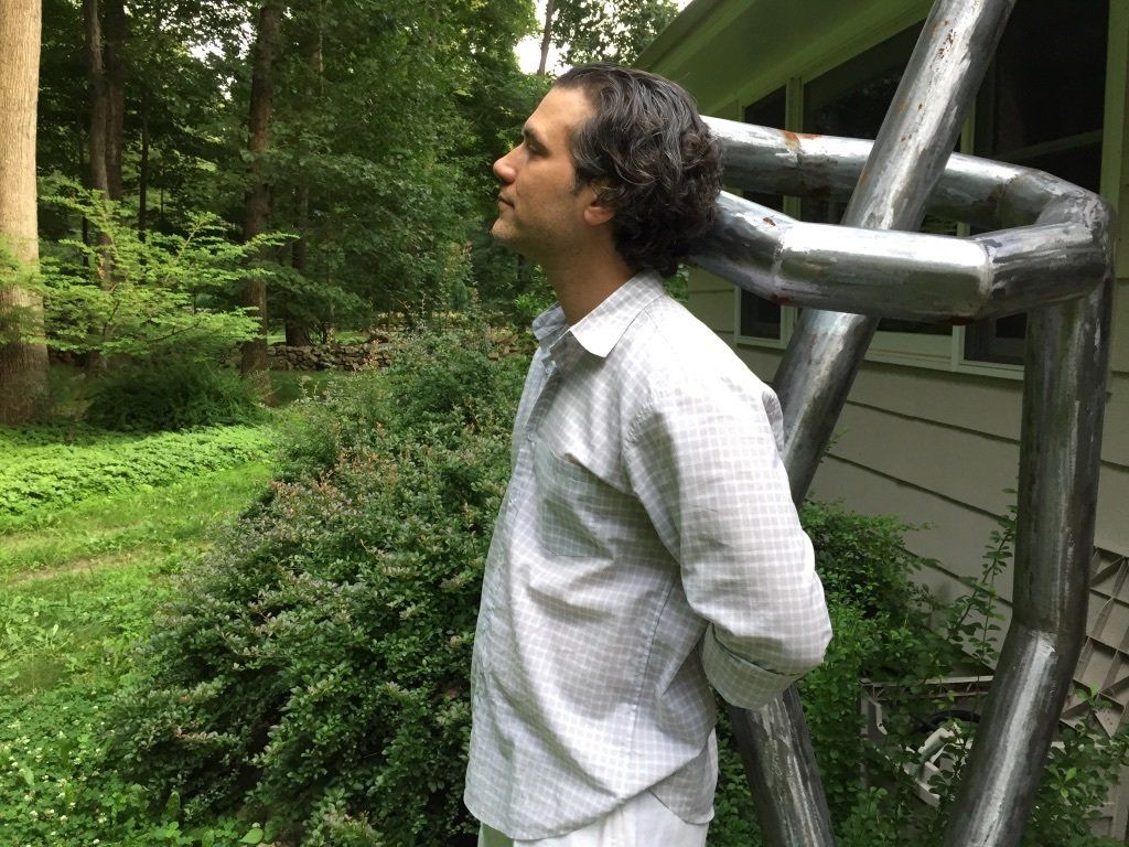 A man in a white shirt is standing in front of a sculpture.