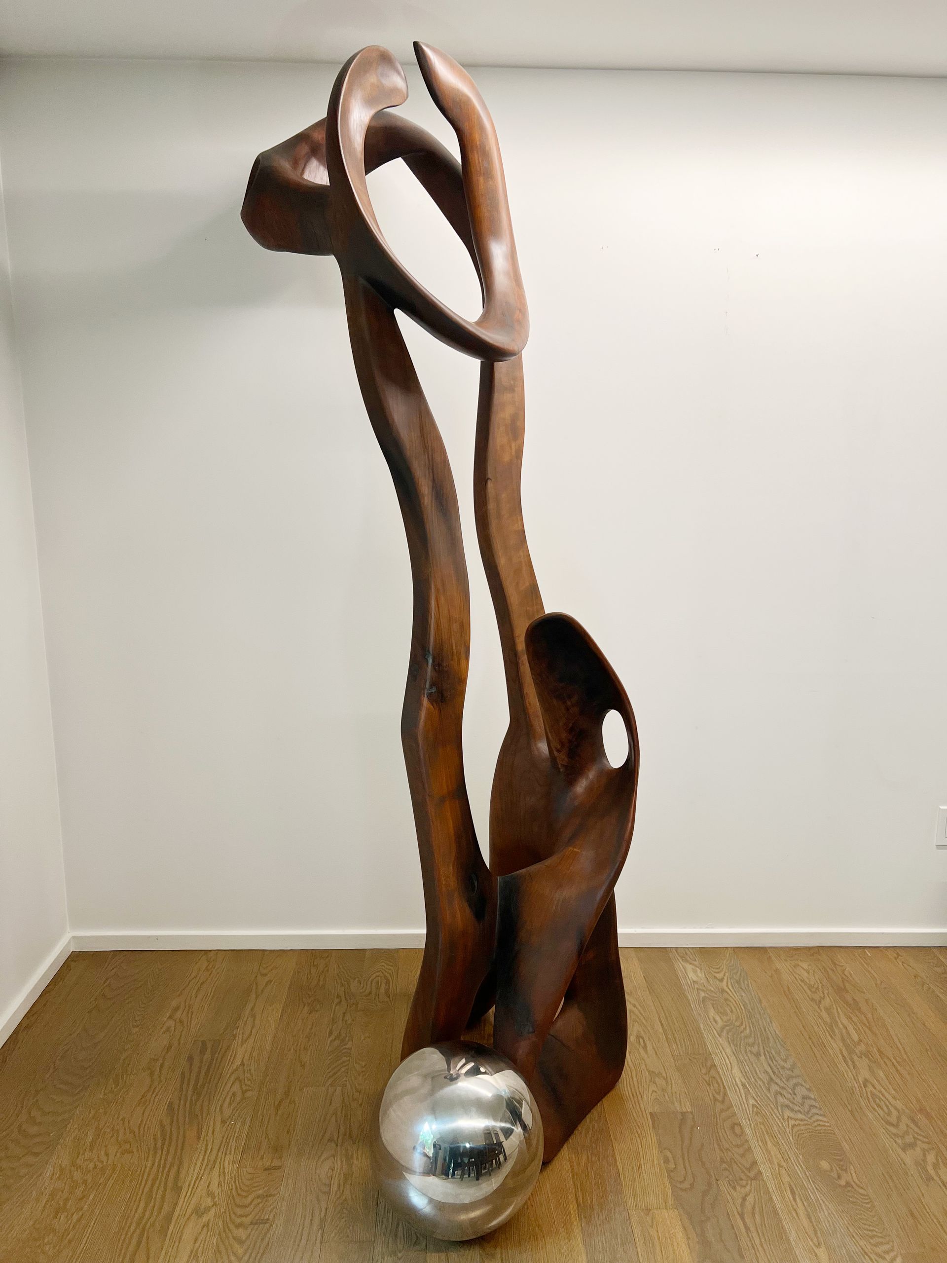A large wooden sculpture is sitting on a white pedestal in a room.