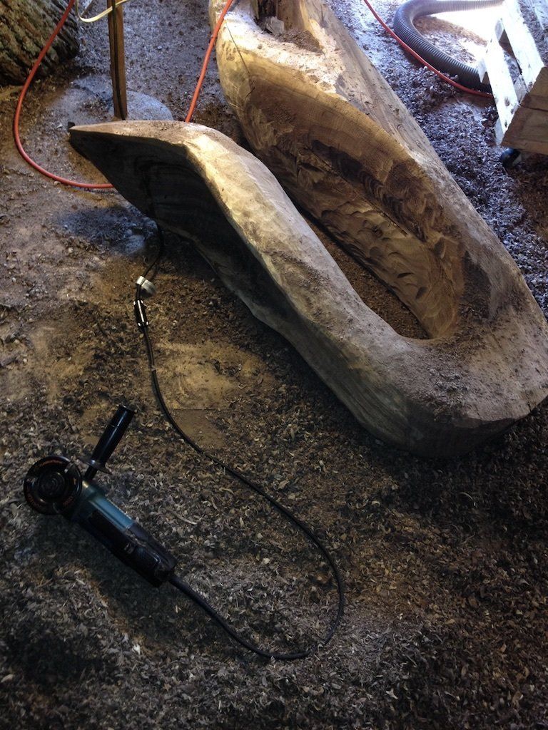 A large piece of wood is sitting on the ground next to a grinder.