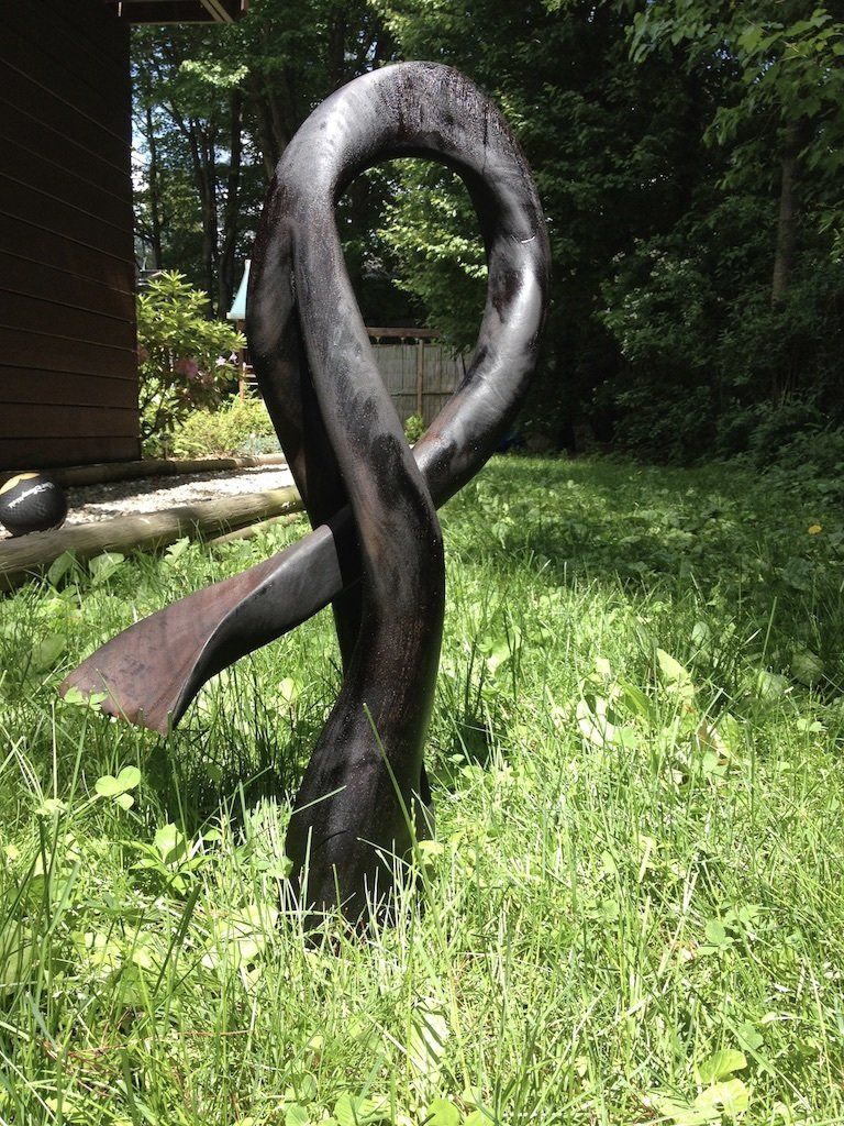 A large black sculpture is sitting in the grass in front of a house