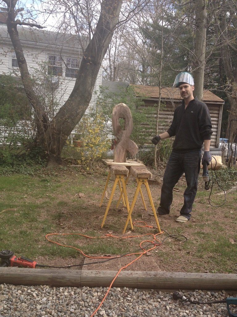 A man is standing next to a wooden sculpture on a workbench.
