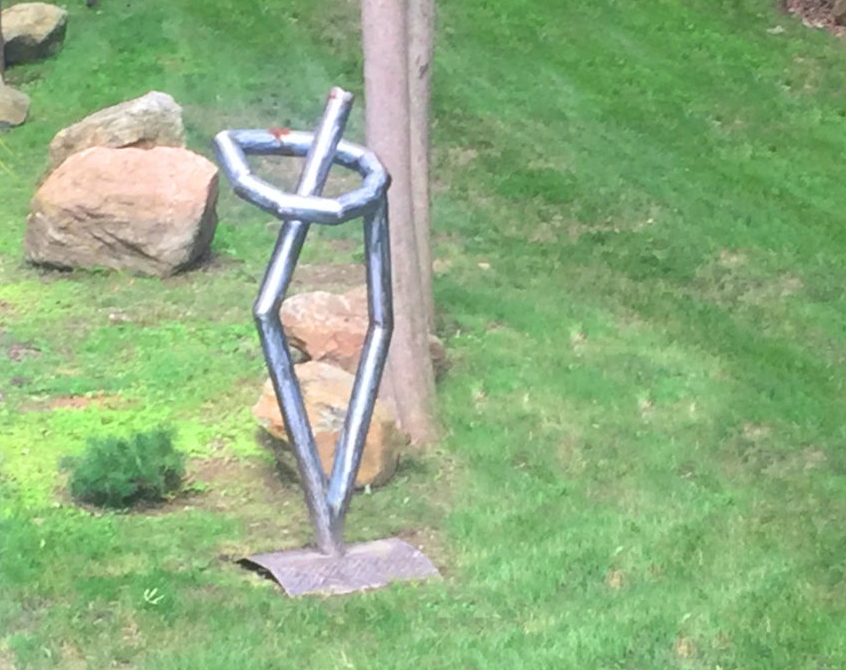 A metal sculpture is sitting in the grass next to a tree.