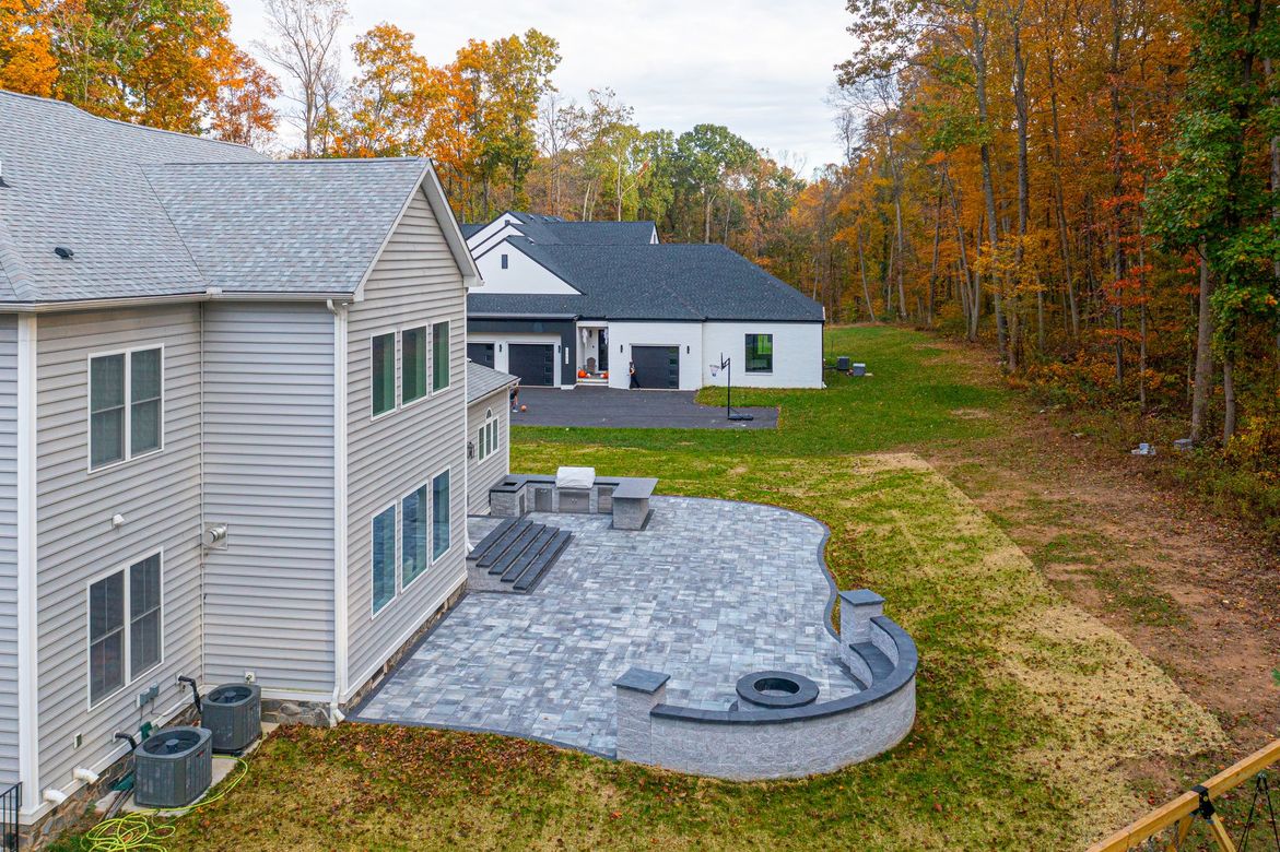 Backyard with stone patio, fire pit, and two houses set in autumn woods.