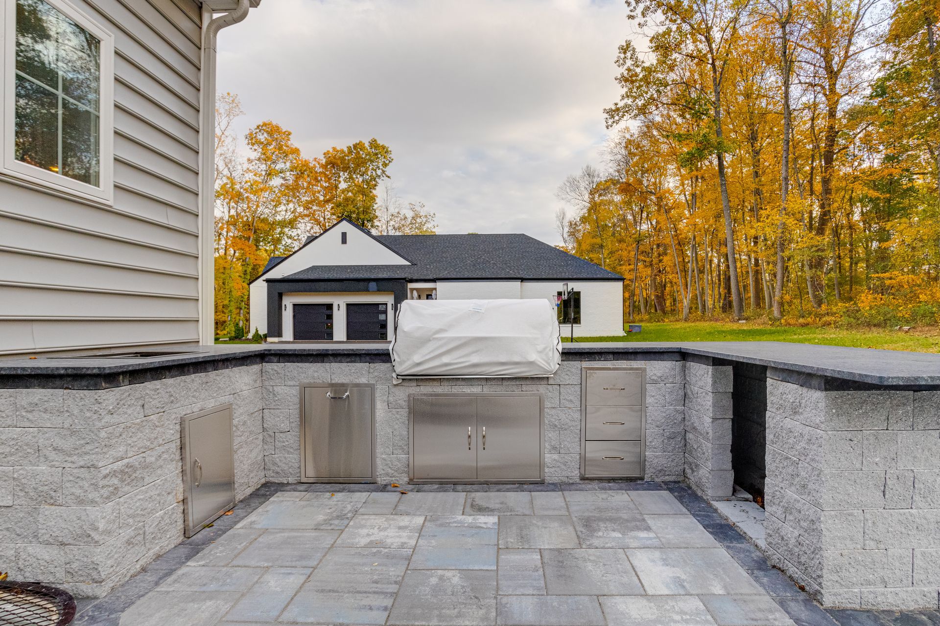 An outdoor stone kitchen area with a covered built-in grill and stainless steel cabinets on a gray stone patio.
