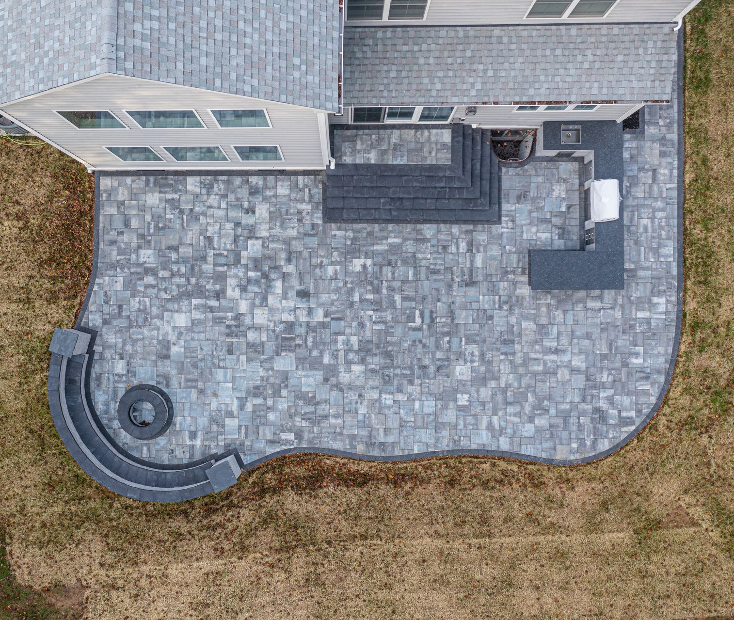 Overhead view of a home's backyard patio with gray pavers, a built-in grill, and fire pit.