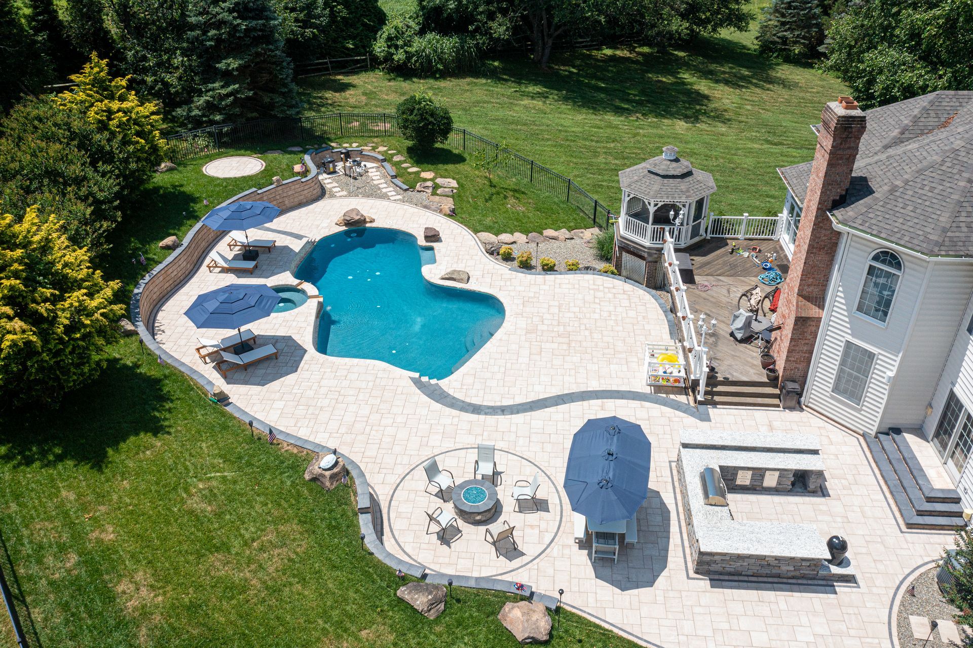 Aerial view of a backyard with a pool, patio, gazebo, and lawn; sunny day.